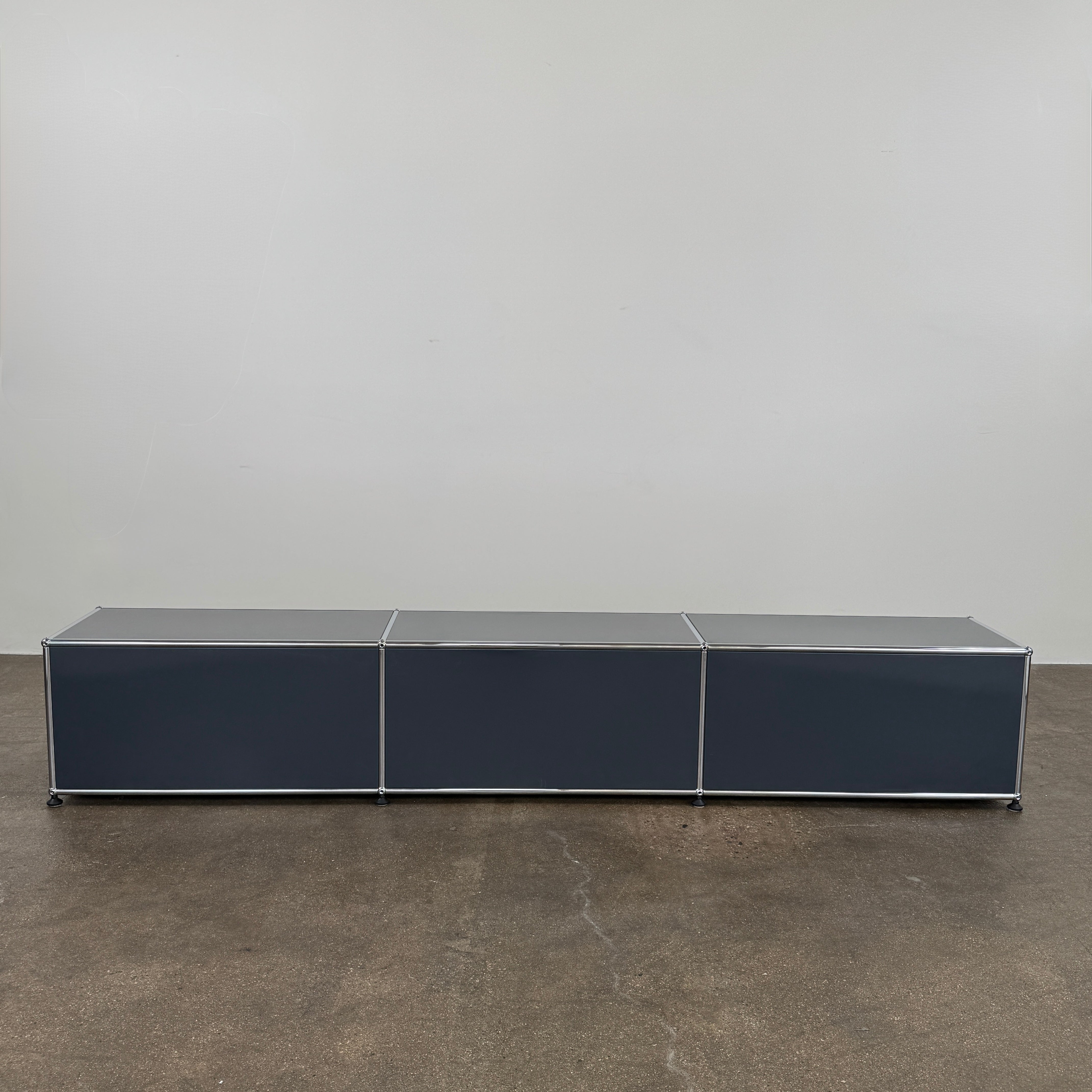 The USM Haller Low Console - Three Flap Door Unit features three black flap doors with round knobs and a silver frame, shown against a plain white background.