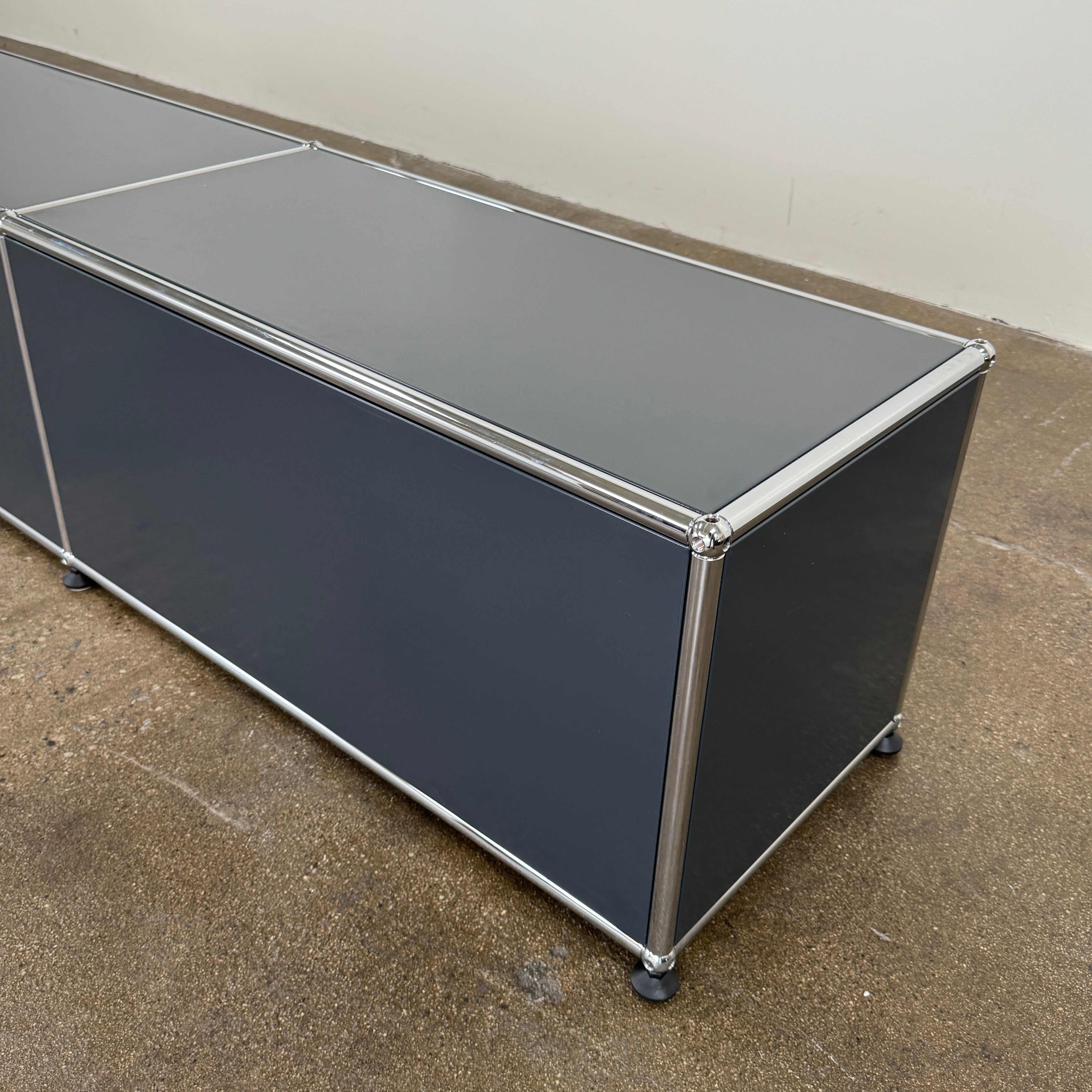 The USM Haller Low Console - Three Flap Door Unit features three black flap doors with round knobs and a silver frame, shown against a plain white background.