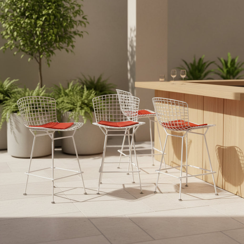 A set of three Bertoia Indoor/Outdoor Counter Stools by Vintage Modern, featuring white welded steel frames with wire backs and bold red seat cushions, lined up in a row against a simple white background—ideal for adding modern style to any indoor or outdoor space.