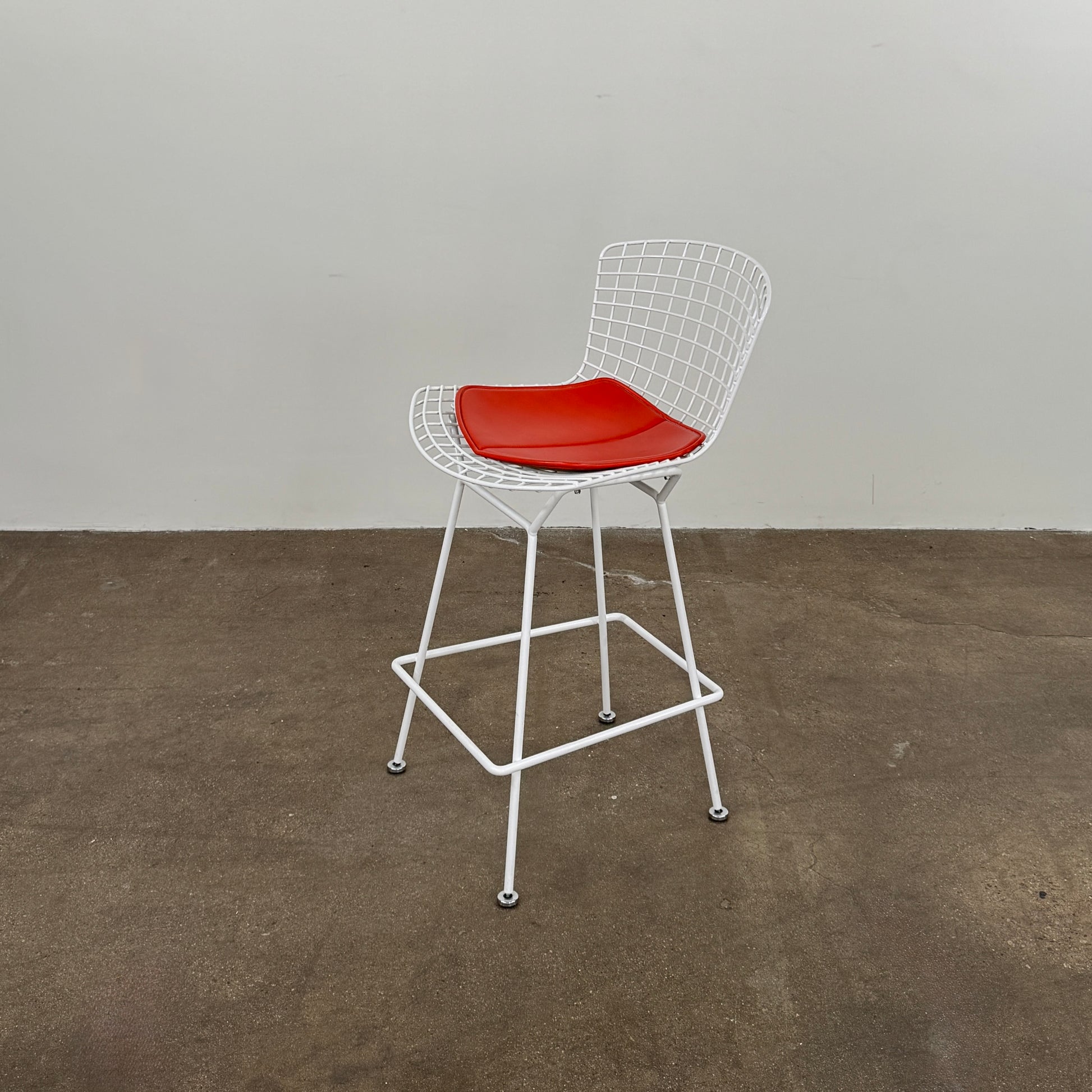 A set of three Bertoia Indoor/Outdoor Counter Stools by Vintage Modern, featuring white welded steel frames with wire backs and bold red seat cushions, lined up in a row against a simple white background—ideal for adding modern style to any indoor or outdoor space.