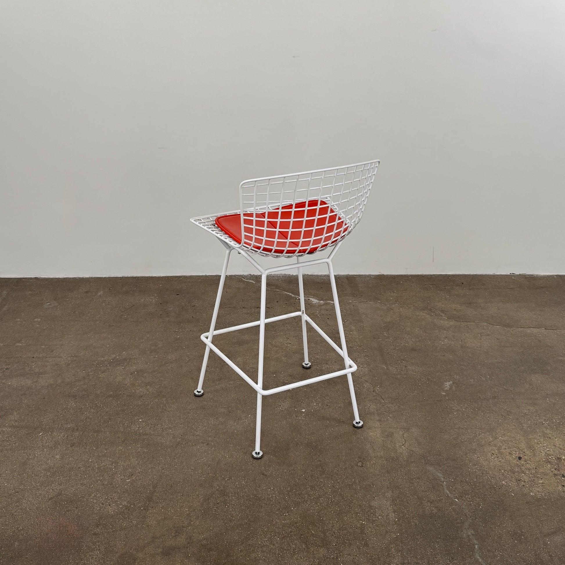 A set of three Bertoia Indoor/Outdoor Counter Stools by Vintage Modern, featuring white welded steel frames with wire backs and bold red seat cushions, lined up in a row against a simple white background—ideal for adding modern style to any indoor or outdoor space.