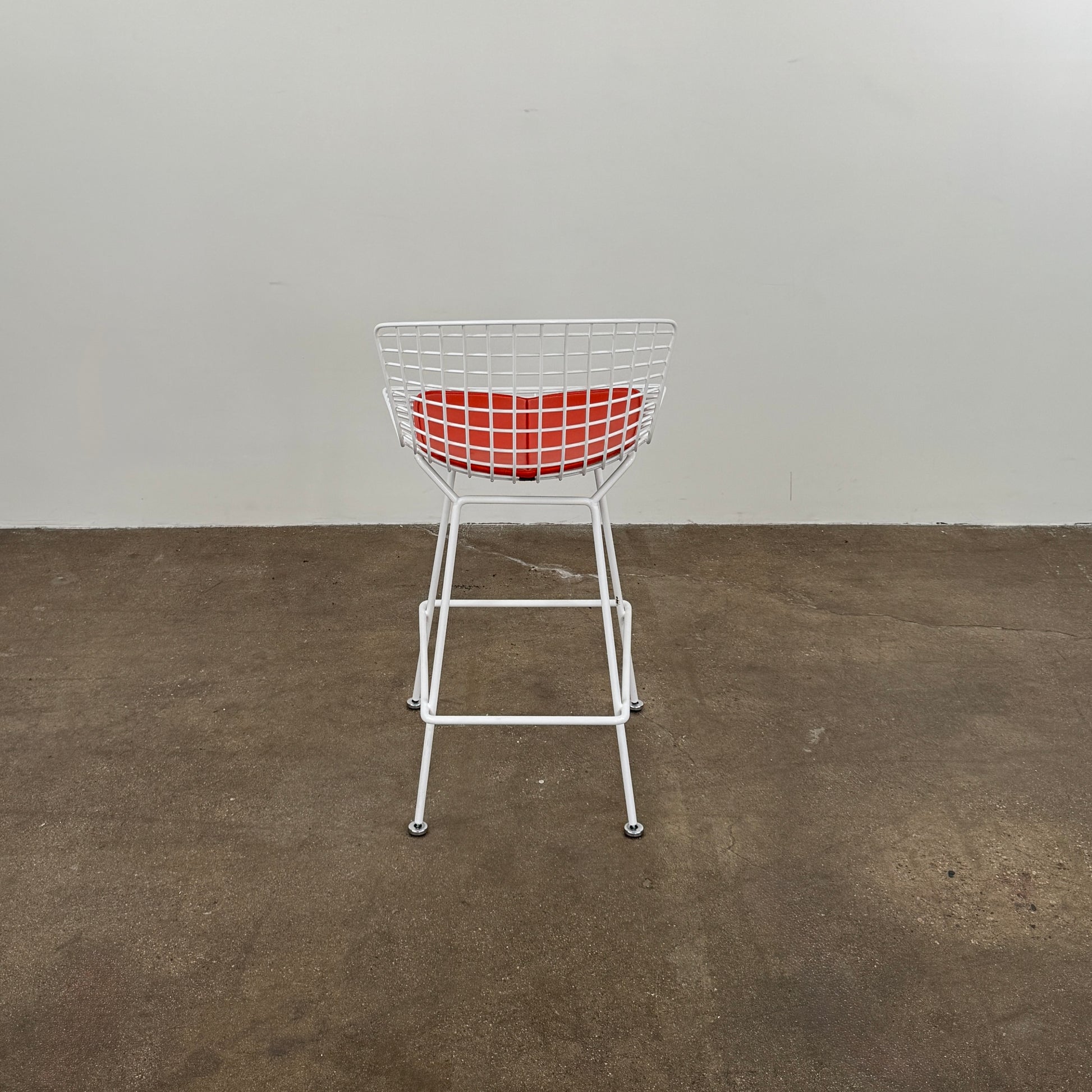 A set of three Bertoia Indoor/Outdoor Counter Stools by Vintage Modern, featuring white welded steel frames with wire backs and bold red seat cushions, lined up in a row against a simple white background—ideal for adding modern style to any indoor or outdoor space.