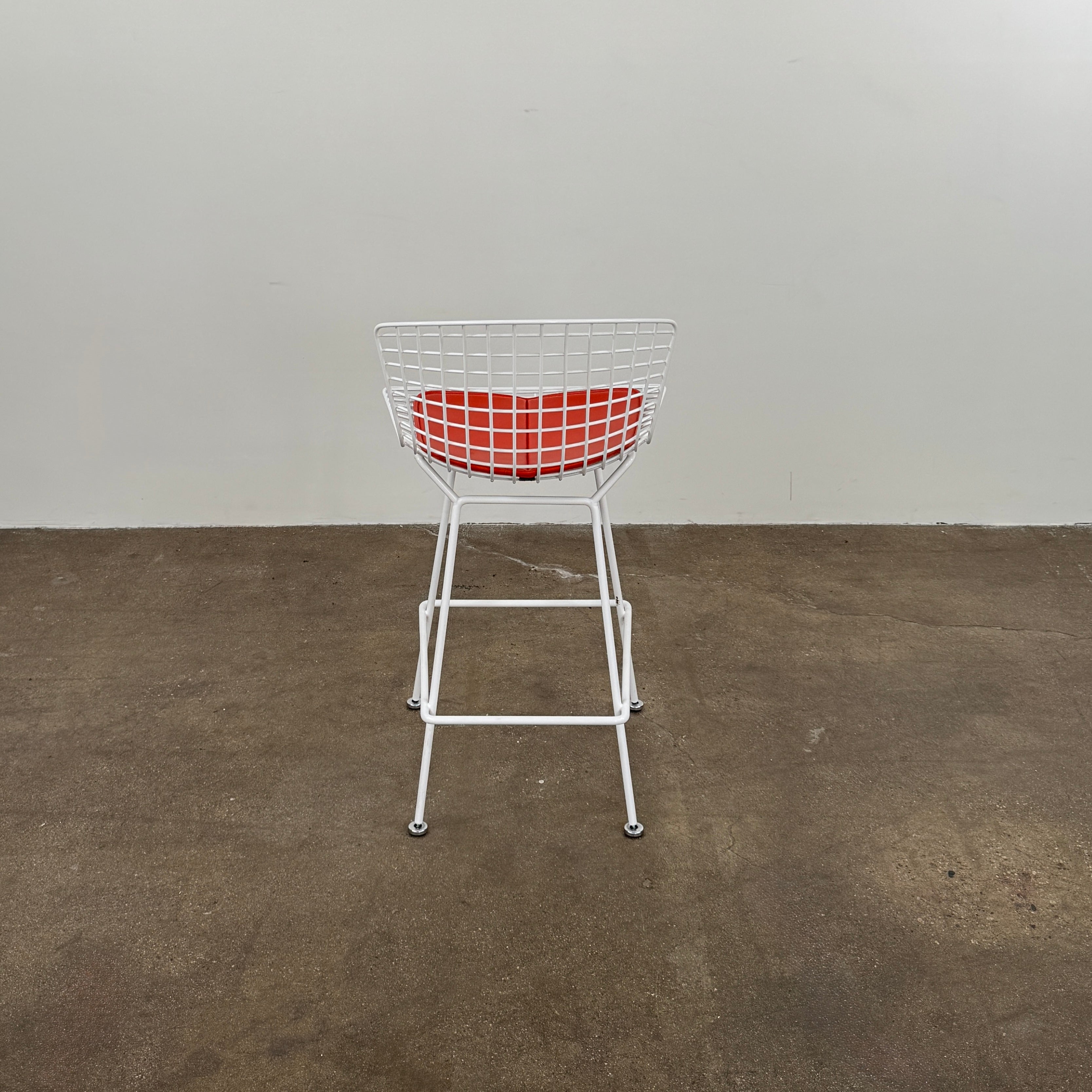 A set of three Bertoia Indoor/Outdoor Counter Stools by Vintage Modern, featuring white welded steel frames with wire backs and bold red seat cushions, lined up in a row against a simple white background—ideal for adding modern style to any indoor or outdoor space.