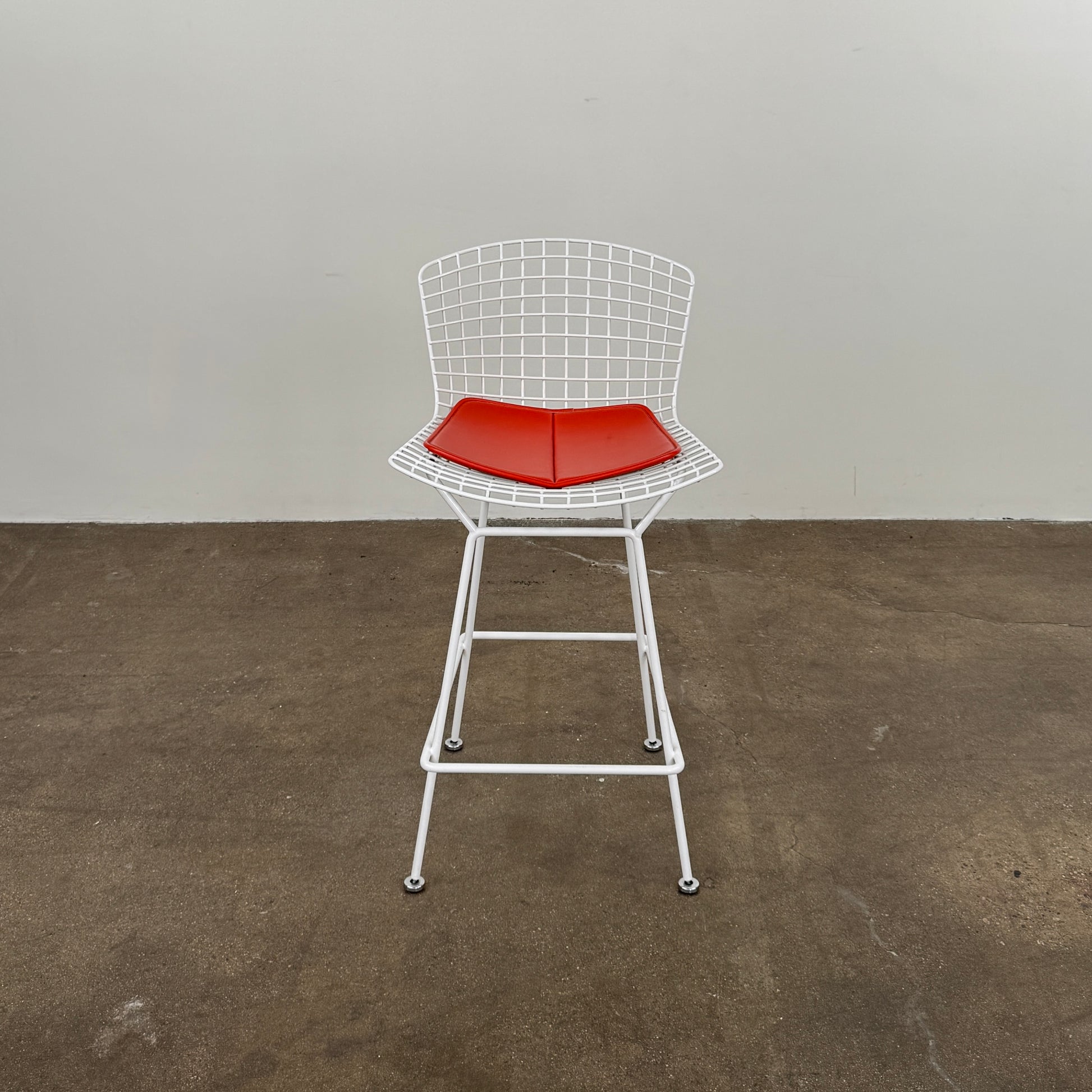 A set of three Bertoia Indoor/Outdoor Counter Stools by Vintage Modern, featuring white welded steel frames with wire backs and bold red seat cushions, lined up in a row against a simple white background—ideal for adding modern style to any indoor or outdoor space.