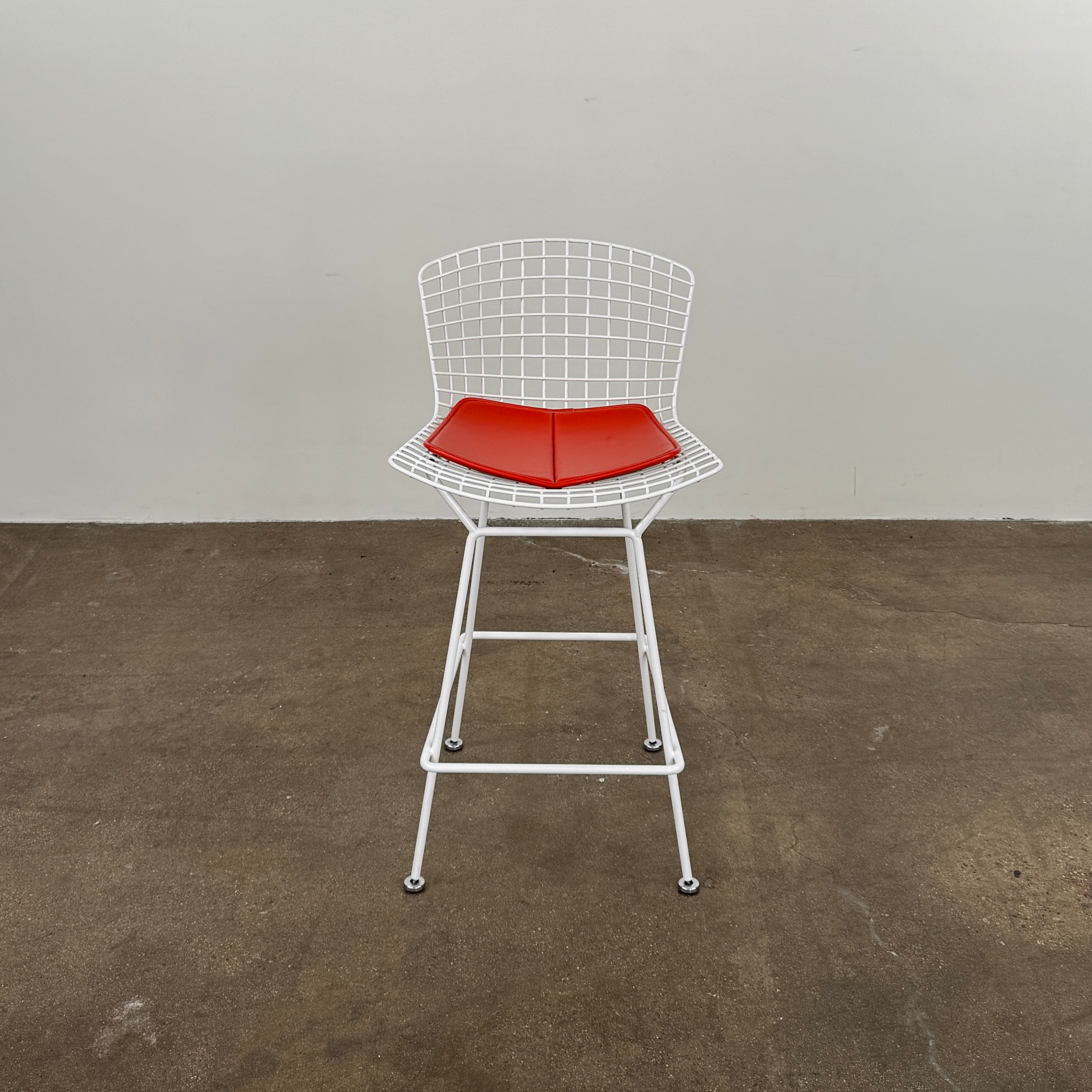 A set of three Bertoia Indoor/Outdoor Counter Stools by Vintage Modern, featuring white welded steel frames with wire backs and bold red seat cushions, lined up in a row against a simple white background—ideal for adding modern style to any indoor or outdoor space.