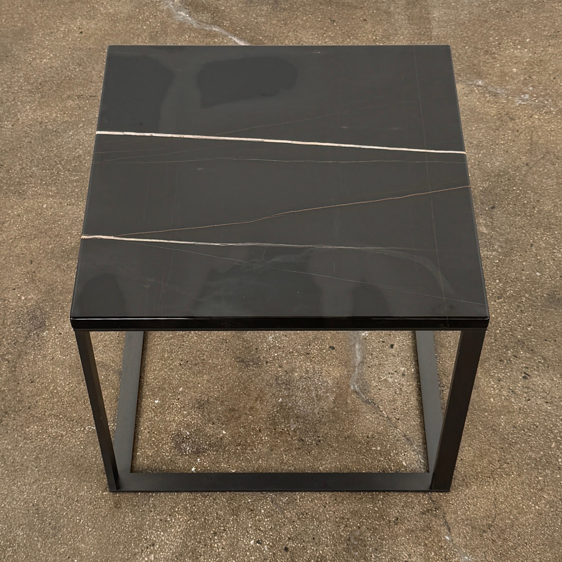The Maxalto Lithos Side Table Sahara Noir Marble Top by Maxalto features a square black frame designed by Antonio Citterio and a marble top with subtle light veining.