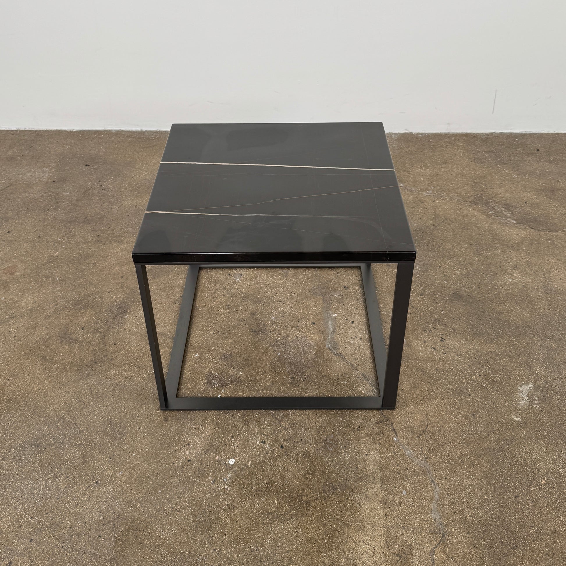 The Maxalto Lithos Side Table Sahara Noir Marble Top by Maxalto features a square black frame designed by Antonio Citterio and a marble top with subtle light veining.