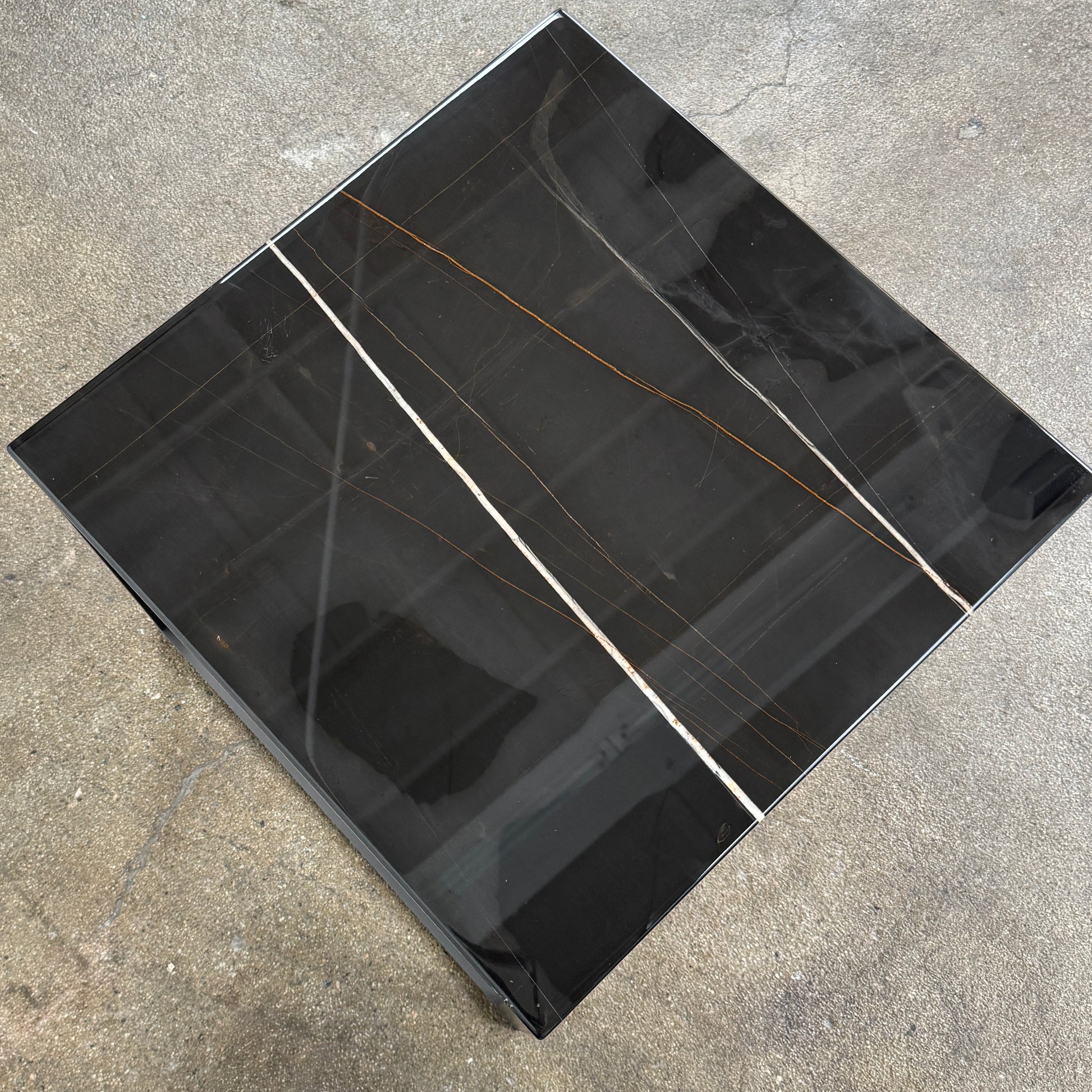 The Maxalto Lithos Side Table Sahara Noir Marble Top by Maxalto features a square black frame designed by Antonio Citterio and a marble top with subtle light veining.