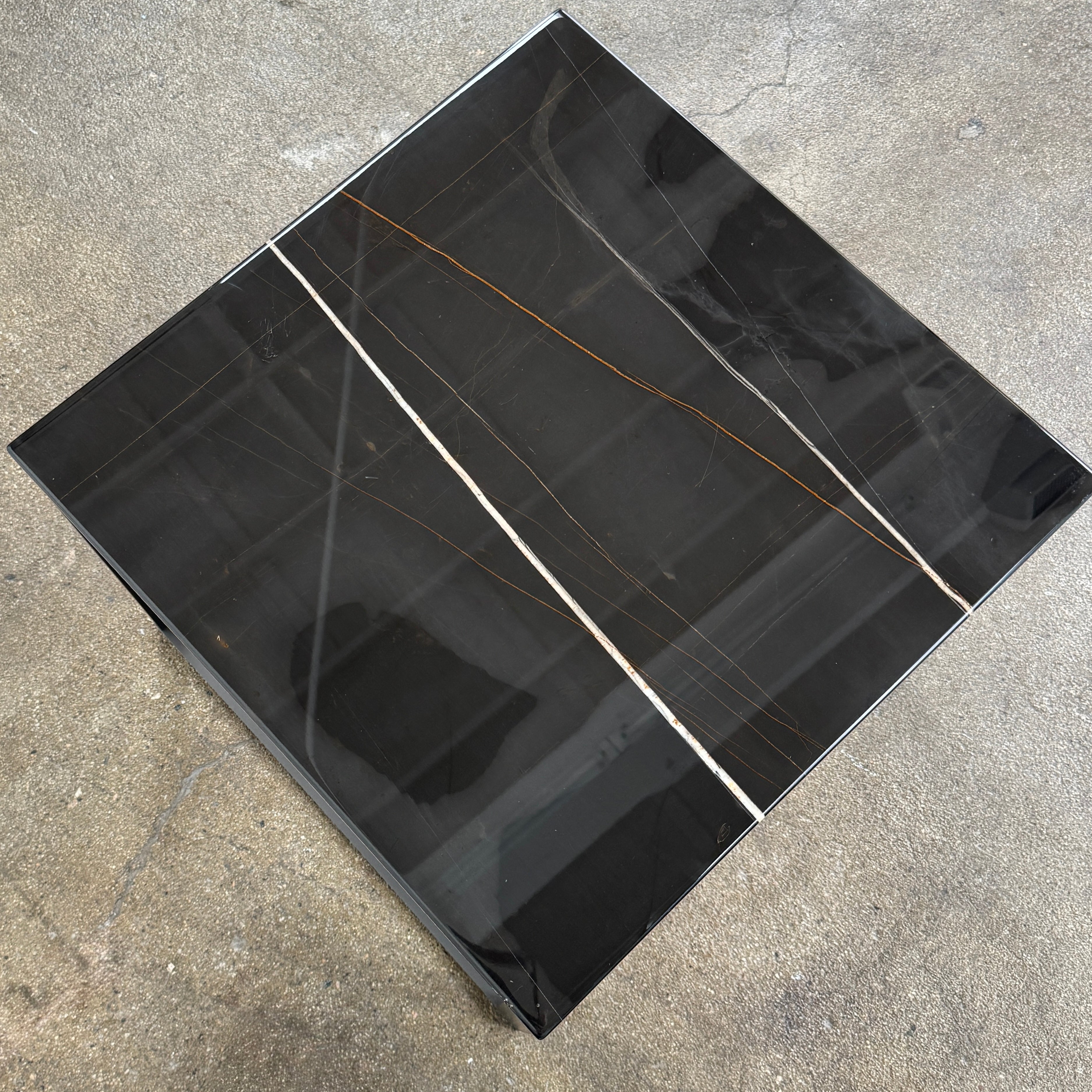 The Maxalto Lithos Side Table Sahara Noir Marble Top by Maxalto features a square black frame designed by Antonio Citterio and a marble top with subtle light veining.
