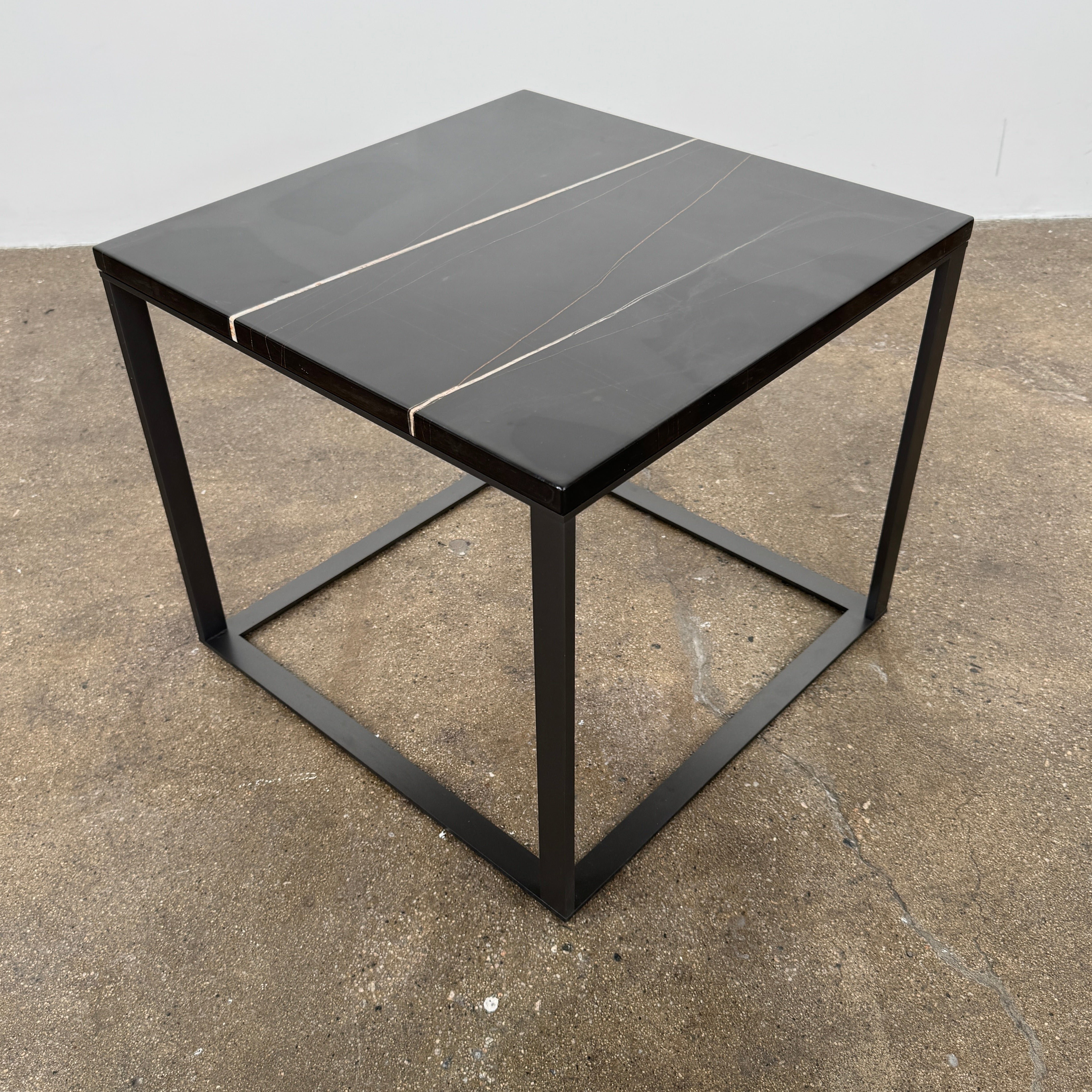 The Maxalto Lithos Side Table Sahara Noir Marble Top by Maxalto features a square black frame designed by Antonio Citterio and a marble top with subtle light veining.