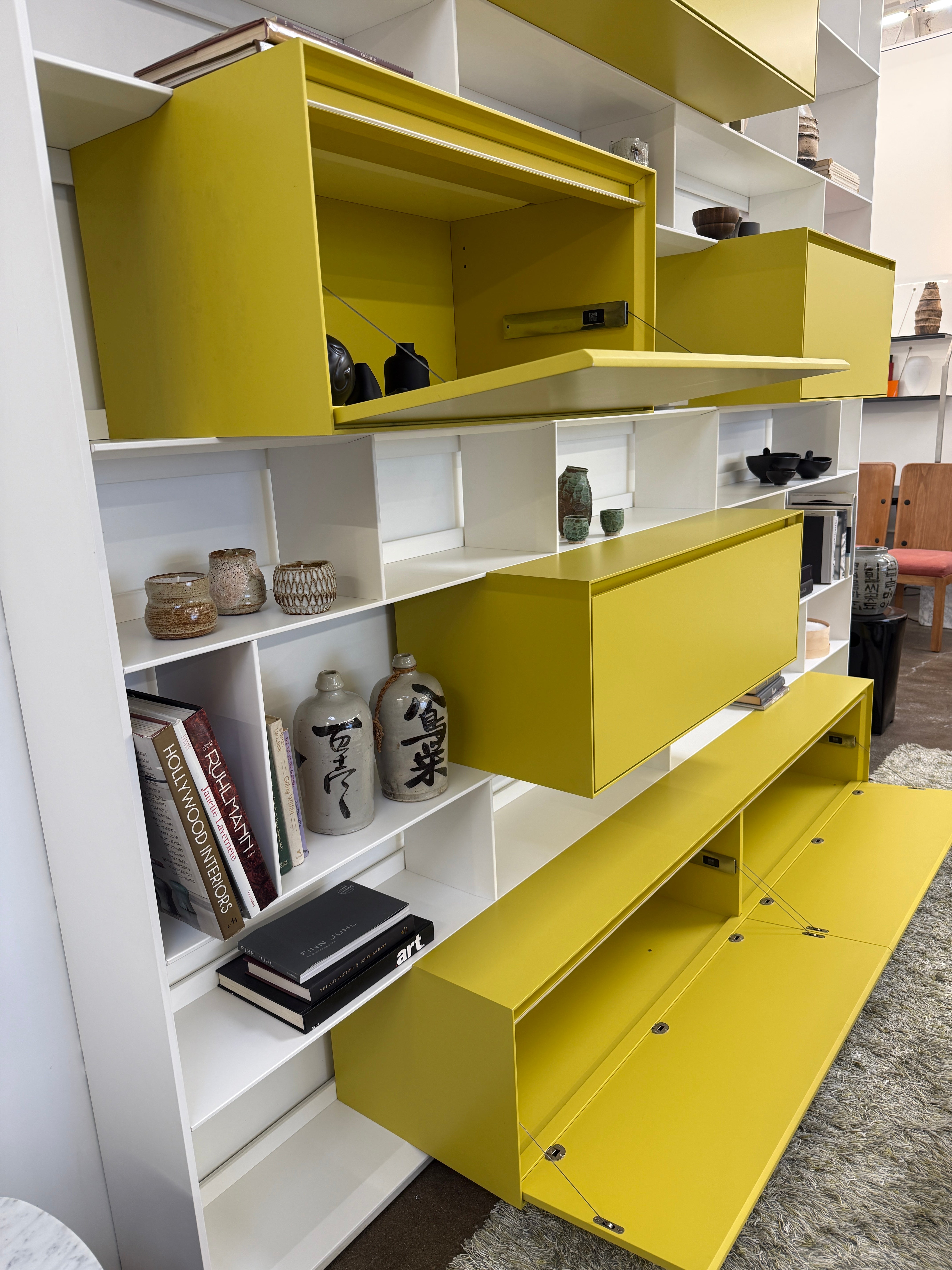 Close-up of a yellow cabinet door with a small paint chip on the bottom edge; black bowls and books are seen on a white shelf of the B&B Italia Flat C Wall Unit With Storage by B&B Italia, combining style and function.