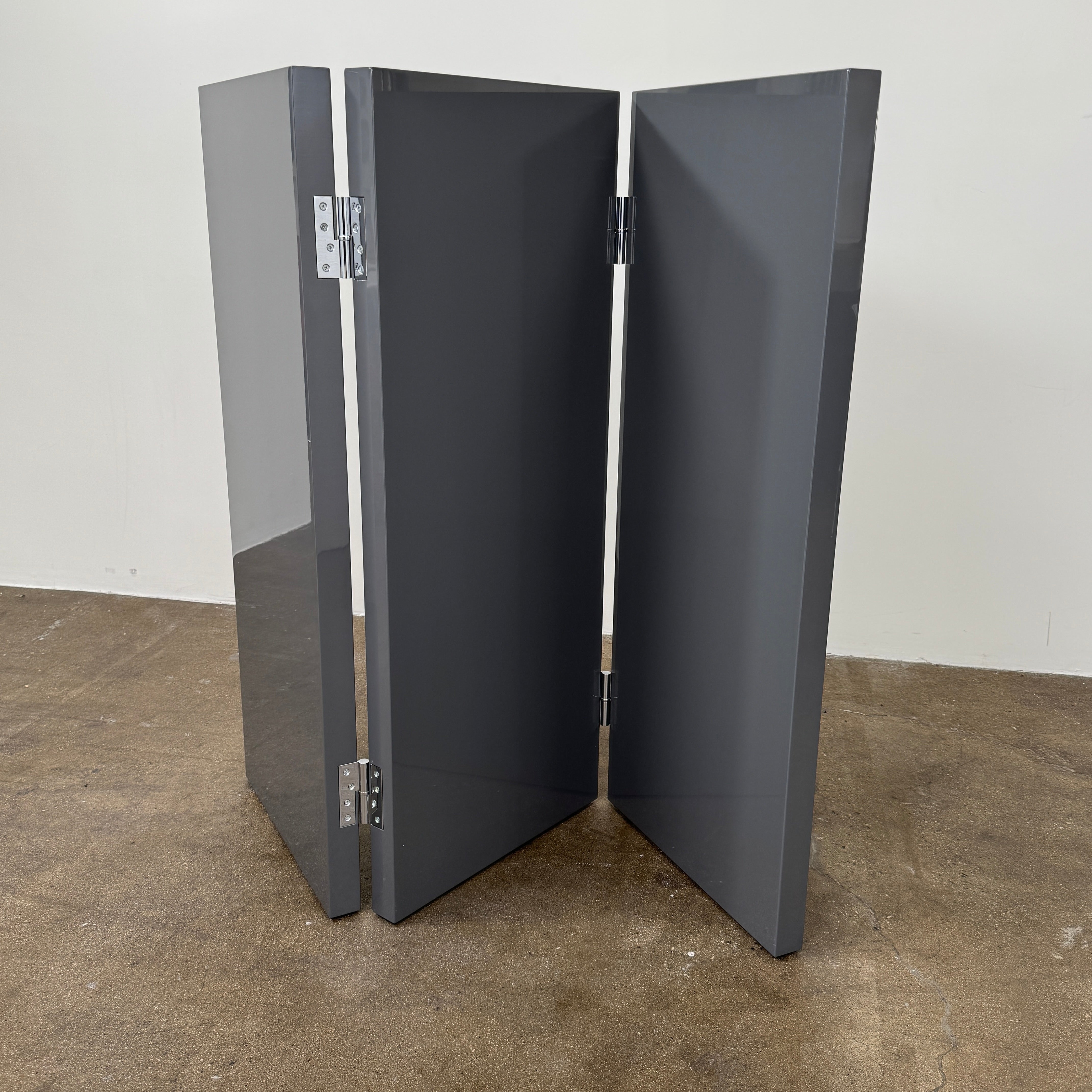 Three large, glossy black rectangular panels connected by metal hinges stand partially folded on a plain background, showcasing the refined sophistication of the Maxalto Arkè 3 Panel Screen by Maxalto—a striking room divider that brings elegant style to any interior.