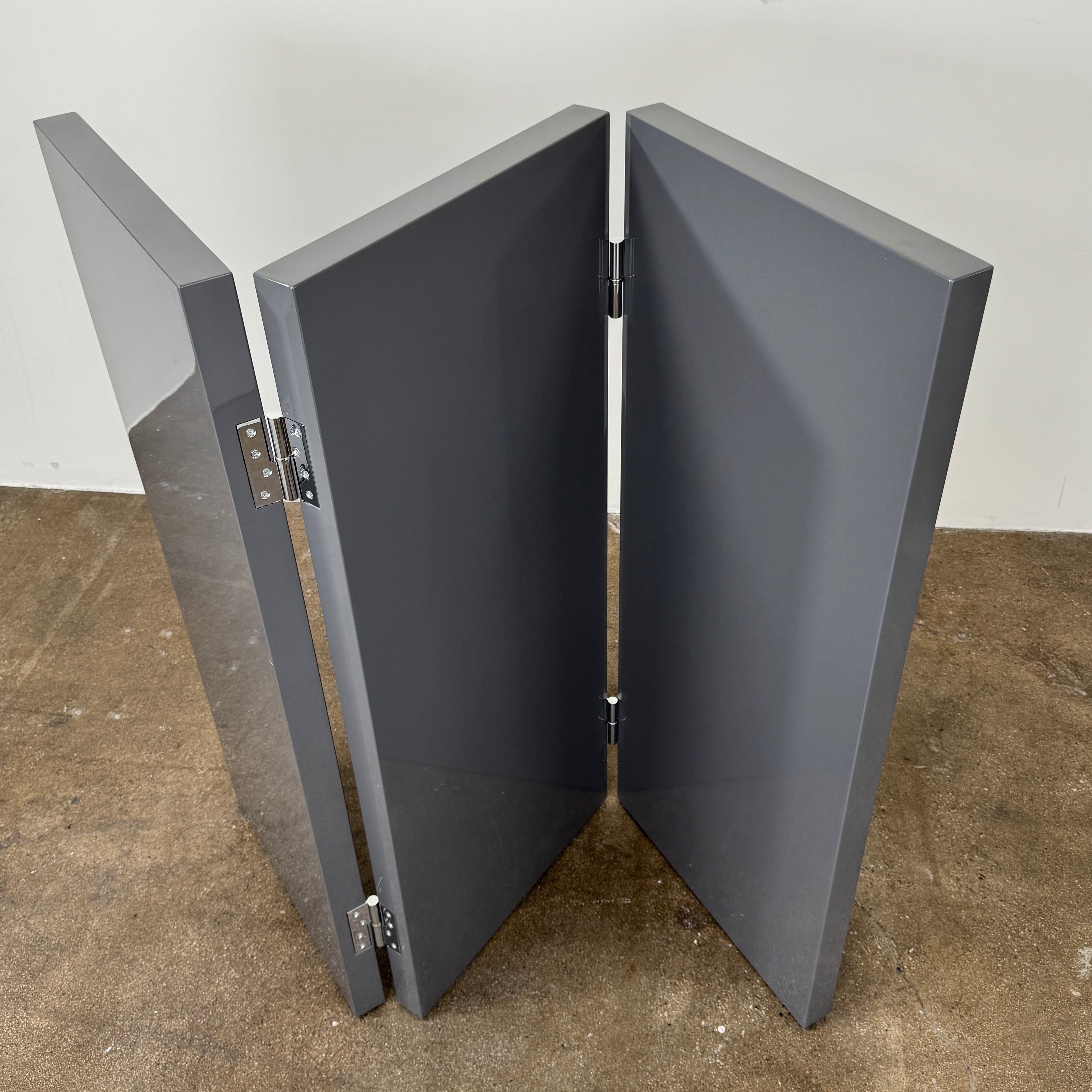 Three large, glossy black rectangular panels connected by metal hinges stand partially folded on a plain background, showcasing the refined sophistication of the Maxalto Arkè 3 Panel Screen by Maxalto—a striking room divider that brings elegant style to any interior.