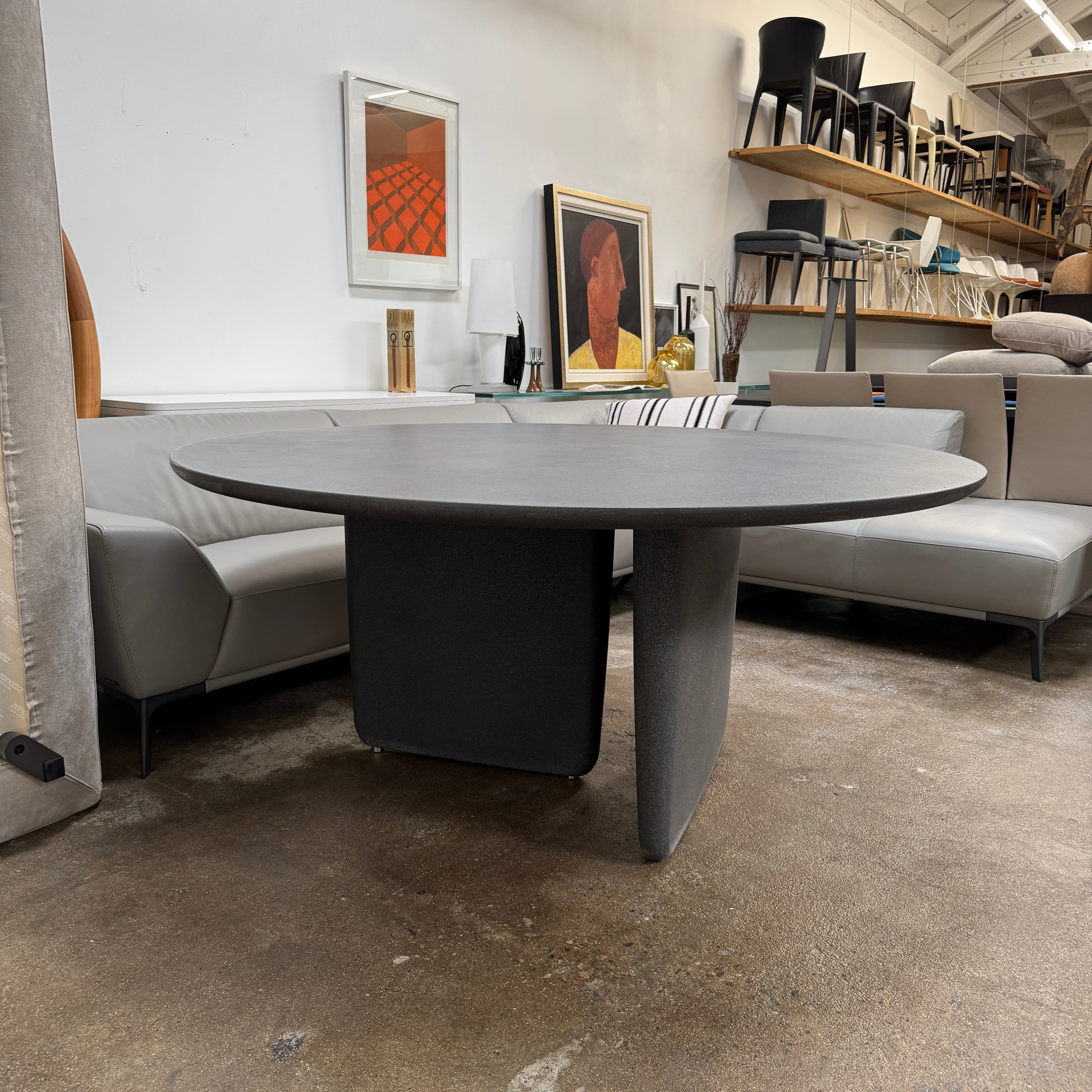 The B&B Italia Tobi-Ishi Outdoor Dining Table by B&B Italia features a modern round black design with a flat top and two asymmetrical base supports, inspired by Zen aesthetics, set against a plain light background.