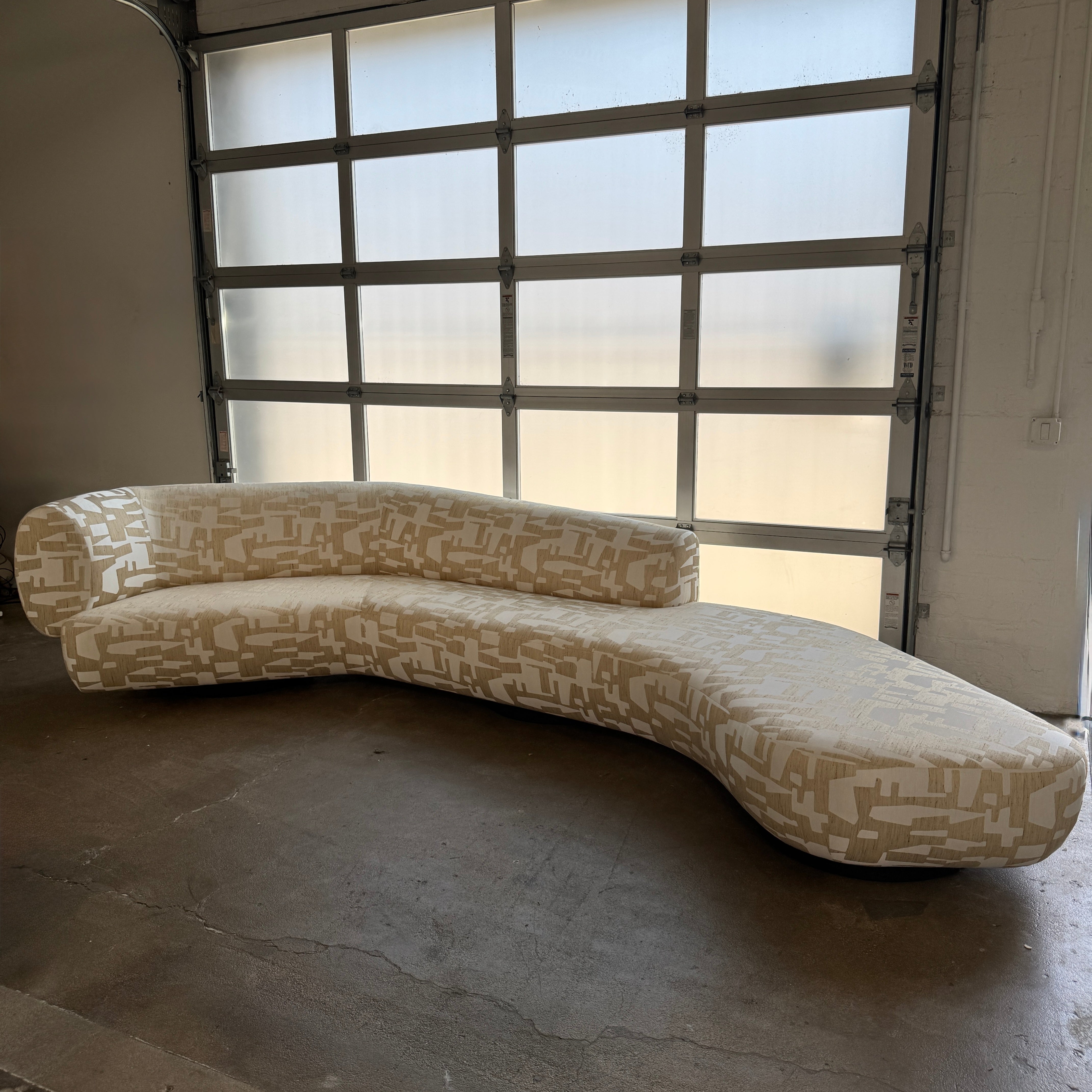 The Muskoka Living Custom Sofa by Muskoka Living showcases an asymmetrical contemporary silhouette with a low backrest, upholstered in luxurious Italian jacquard fabric featuring an abstract geometric pattern in beige, and is presented against a plain white background.