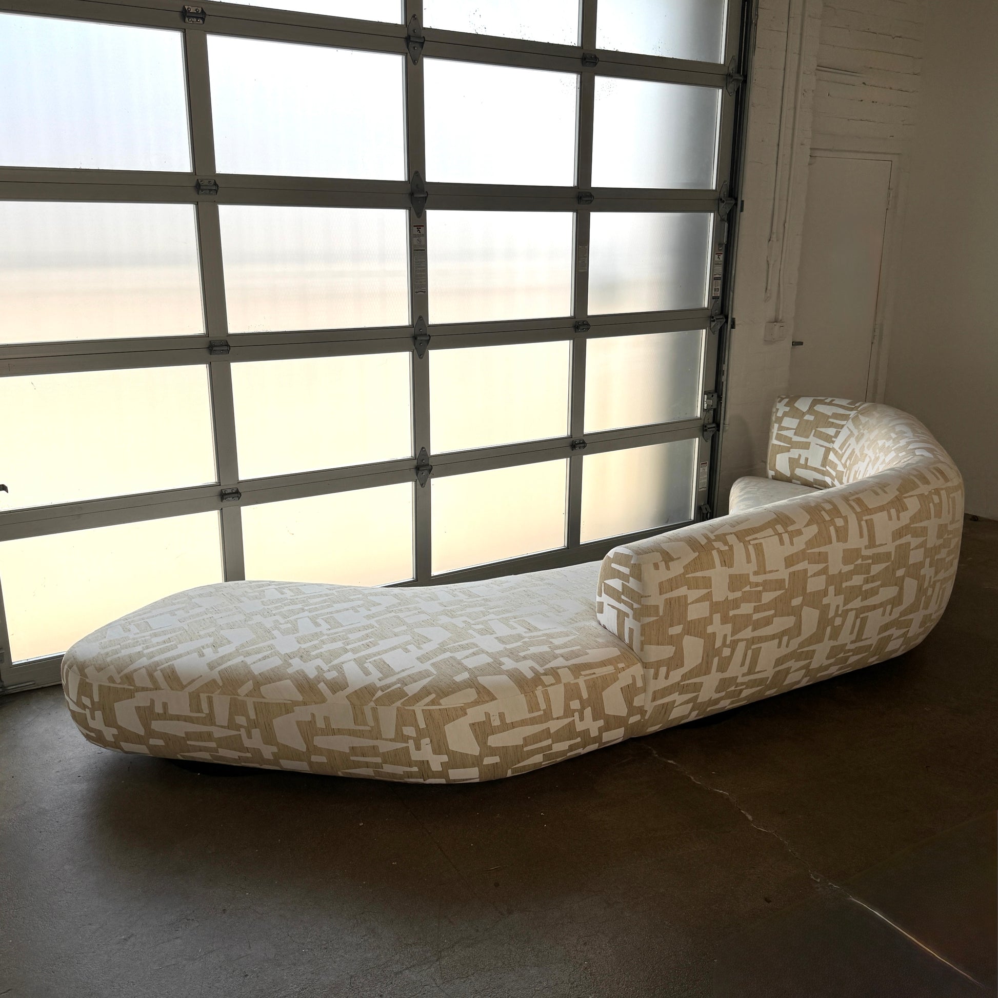 The Muskoka Living Custom Sofa by Muskoka Living showcases an asymmetrical contemporary silhouette with a low backrest, upholstered in luxurious Italian jacquard fabric featuring an abstract geometric pattern in beige, and is presented against a plain white background.