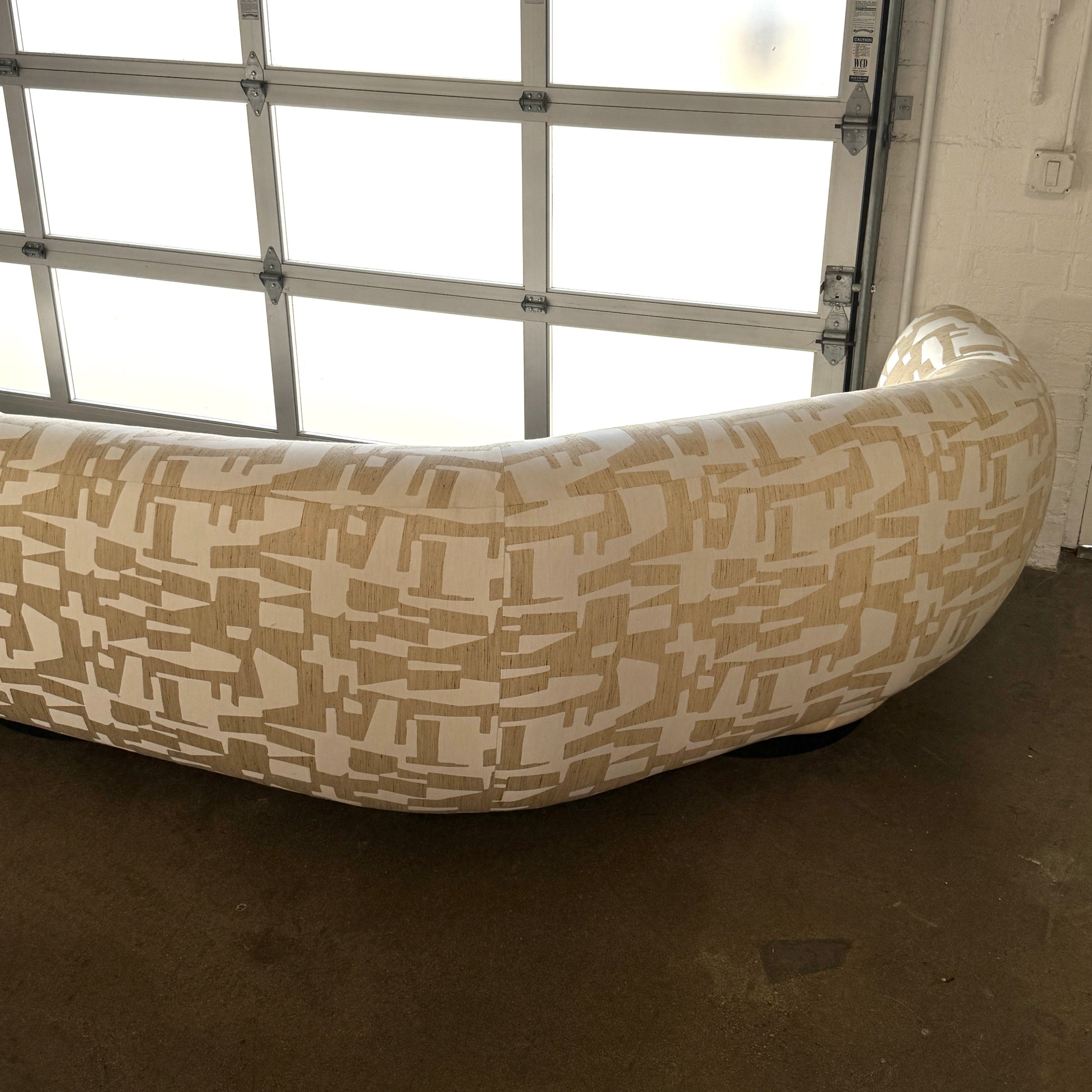 The Muskoka Living Custom Sofa by Muskoka Living showcases an asymmetrical contemporary silhouette with a low backrest, upholstered in luxurious Italian jacquard fabric featuring an abstract geometric pattern in beige, and is presented against a plain white background.