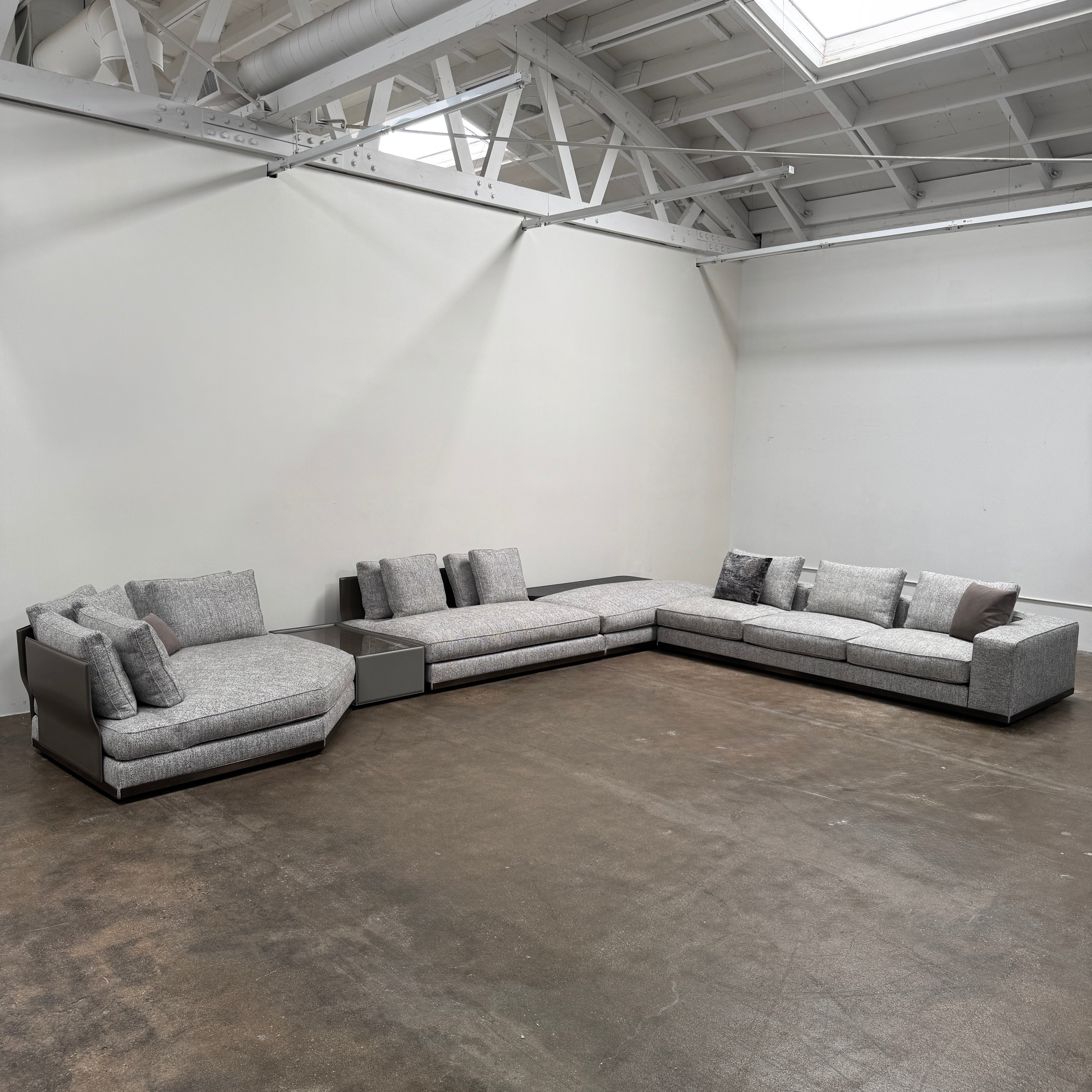 The Minotti West Sectional Sofa with Side Table and Clive Bench by Minotti features a large, L-shaped modern design with gray upholstery, multiple plush cushions, and an integrated side table—perfect for elevating luxury living rooms—all set against a plain white background.
