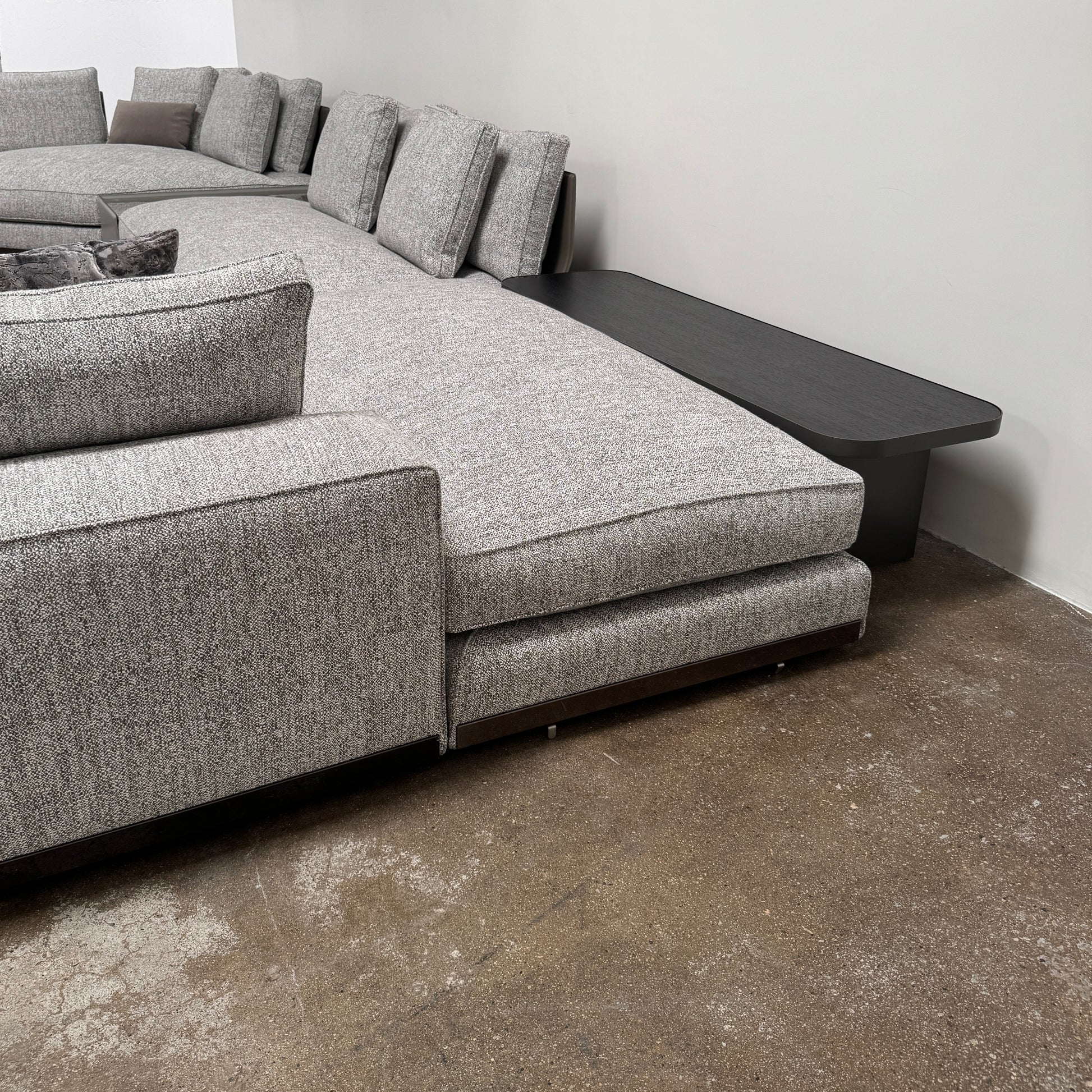 The Minotti West Sectional Sofa with Side Table and Clive Bench by Minotti features a large, L-shaped modern design with gray upholstery, multiple plush cushions, and an integrated side table—perfect for elevating luxury living rooms—all set against a plain white background.