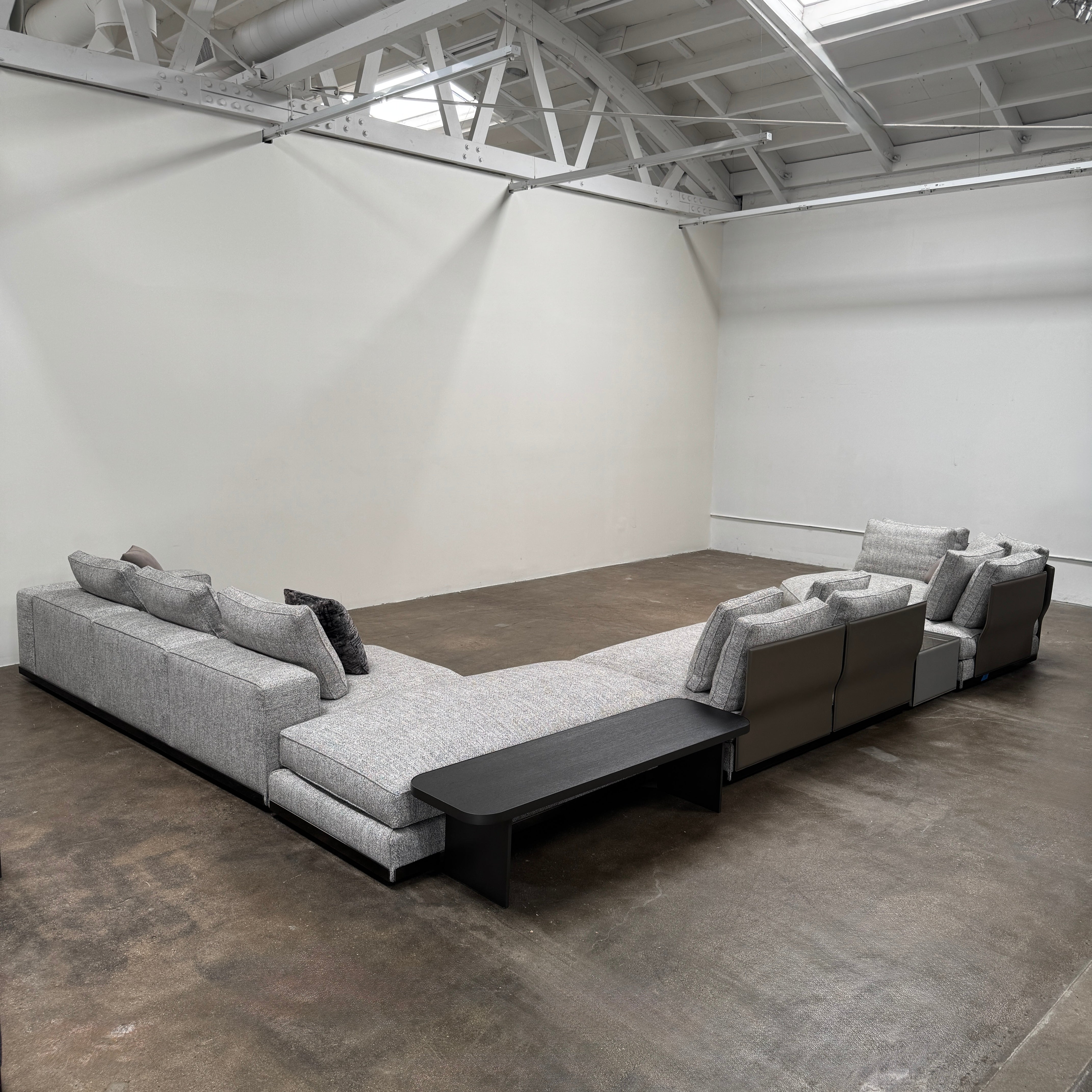The Minotti West Sectional Sofa with Side Table and Clive Bench by Minotti features a large, L-shaped modern design with gray upholstery, multiple plush cushions, and an integrated side table—perfect for elevating luxury living rooms—all set against a plain white background.