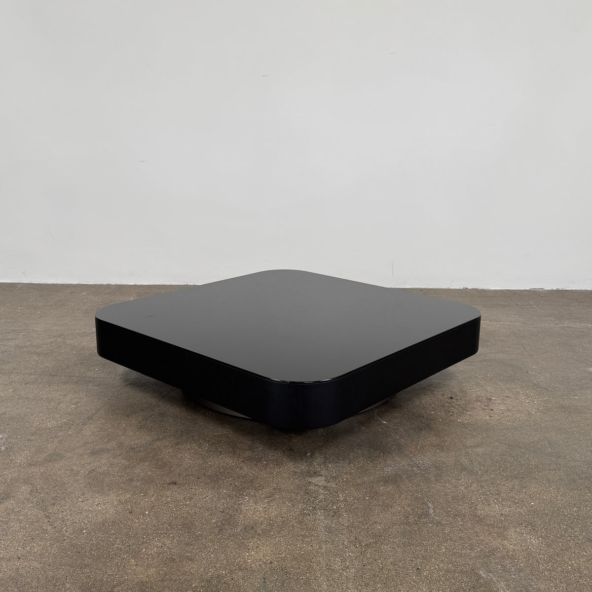 The Minotti Milton Coffee Table by Minotti, featuring a low, square silhouette with rounded corners and a flat surface, stands against a plain white background and embodies contemporary design with an understated sculptural elegance.