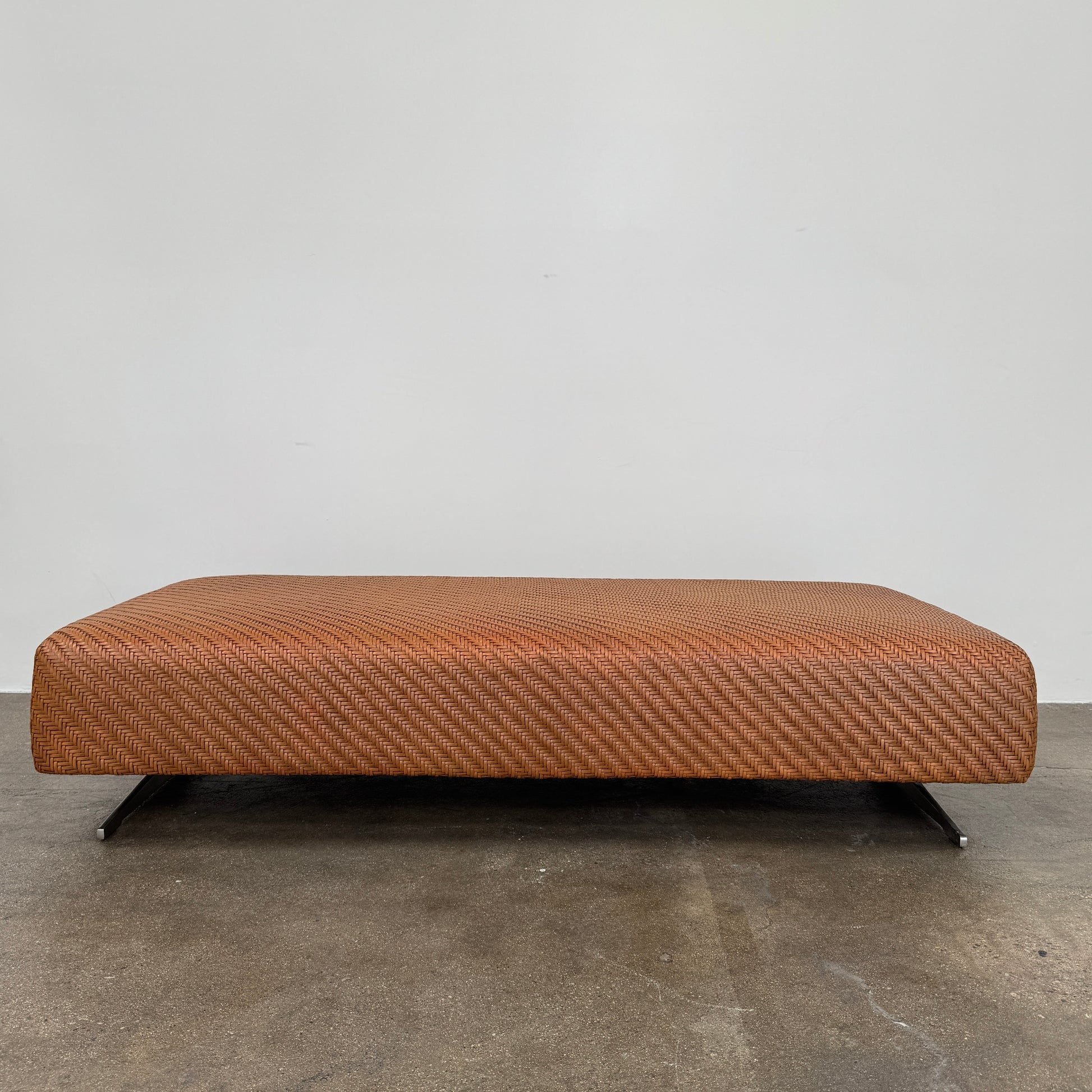 Flexform Filicudi Woven Pouf by Flexform, a rectangular orange bench with a low backless design and metal legs, displayed against a plain white background. Inspired by the iconic Filicudi collection, this elegant piece showcases a distinctive herringbone weave that adds texture and sophistication.
