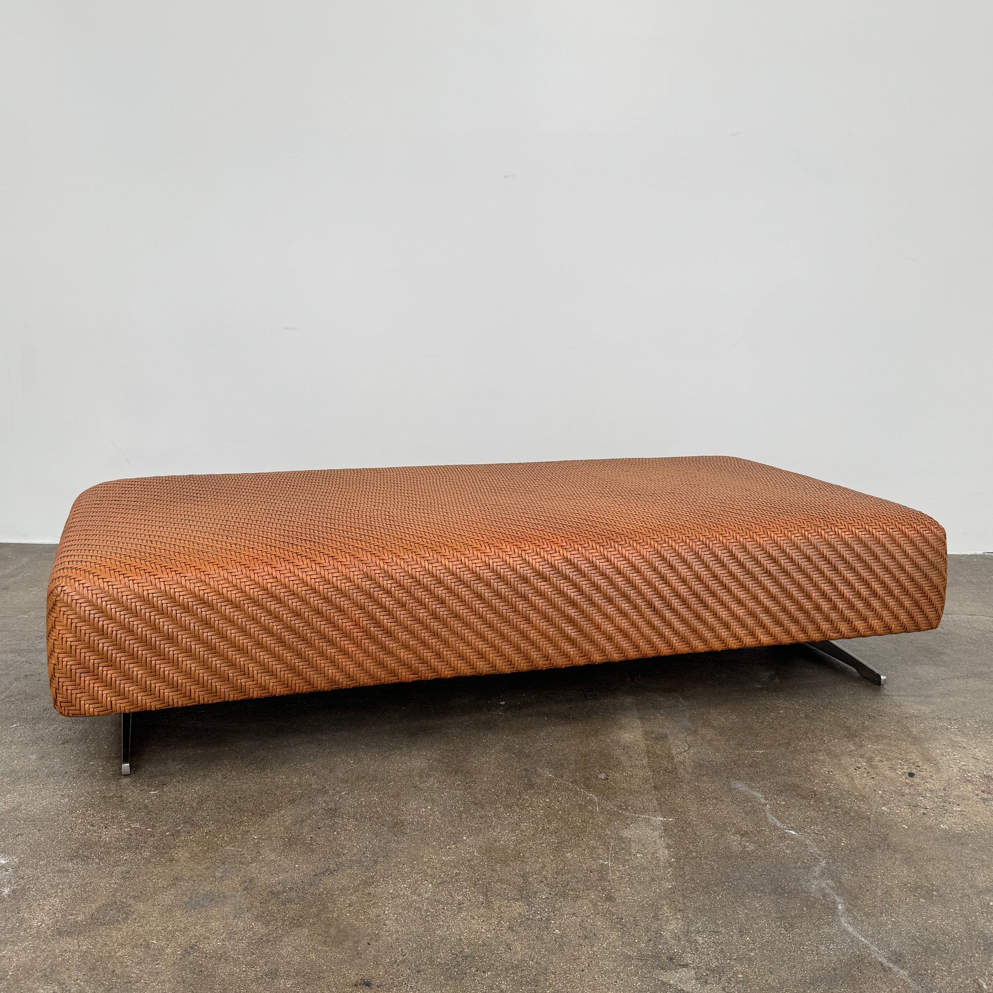 Flexform Filicudi Woven Pouf by Flexform, a rectangular orange bench with a low backless design and metal legs, displayed against a plain white background. Inspired by the iconic Filicudi collection, this elegant piece showcases a distinctive herringbone weave that adds texture and sophistication.
