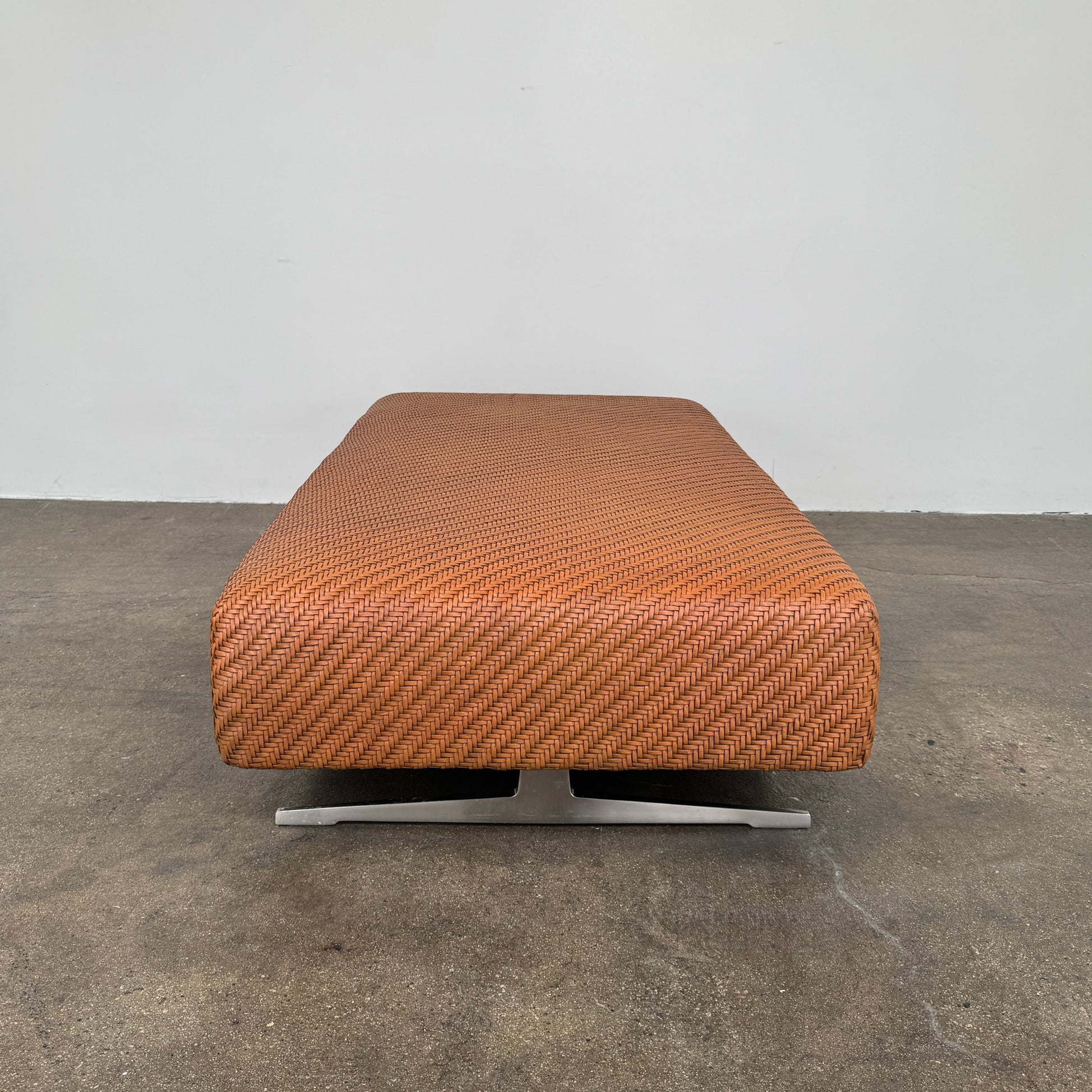 Flexform Filicudi Woven Pouf by Flexform, a rectangular orange bench with a low backless design and metal legs, displayed against a plain white background. Inspired by the iconic Filicudi collection, this elegant piece showcases a distinctive herringbone weave that adds texture and sophistication.
