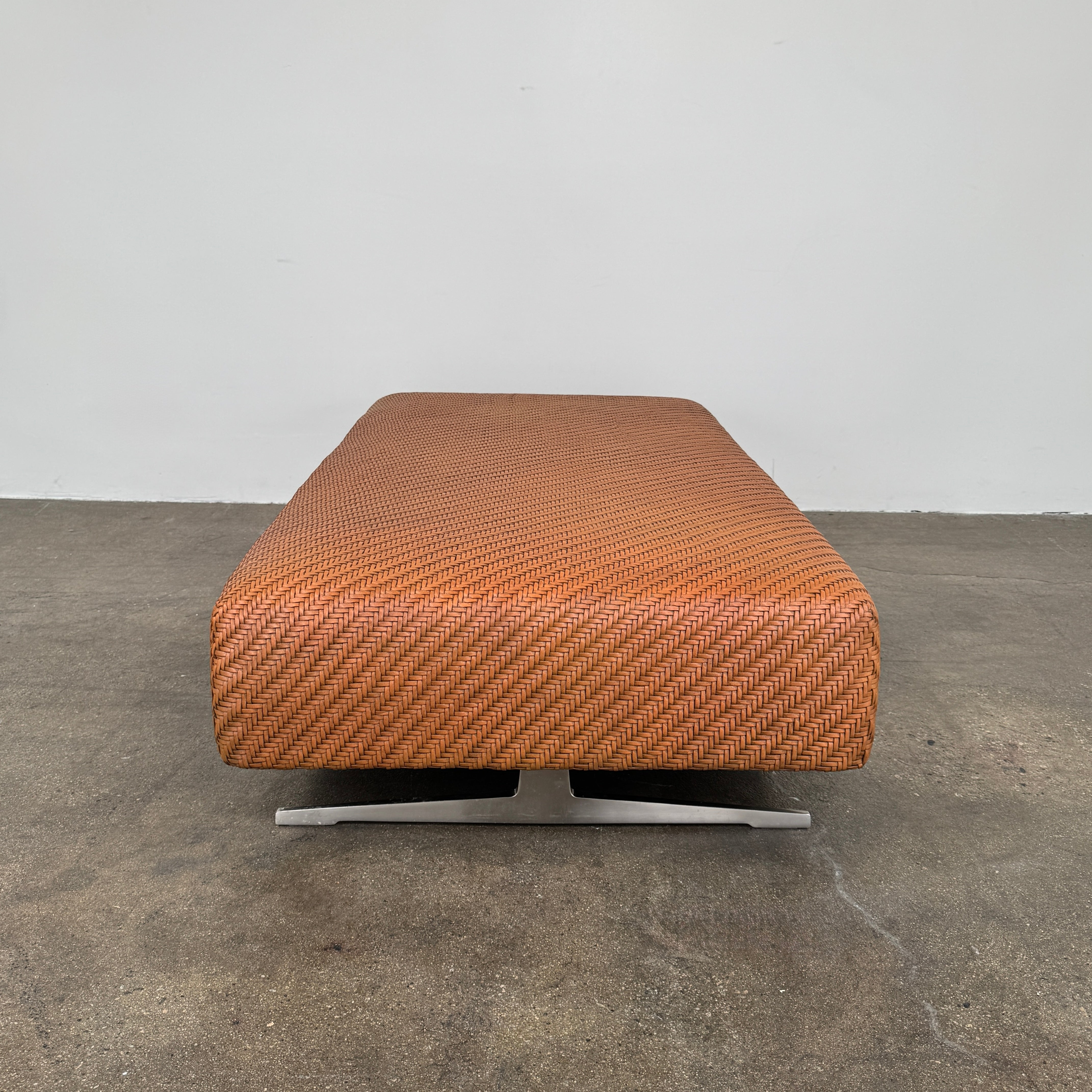 Flexform Filicudi Woven Pouf by Flexform, a rectangular orange bench with a low backless design and metal legs, displayed against a plain white background. Inspired by the iconic Filicudi collection, this elegant piece showcases a distinctive herringbone weave that adds texture and sophistication.