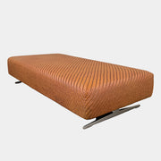 Flexform Filicudi Woven Pouf by Flexform, a rectangular orange bench with a low backless design and metal legs, displayed against a plain white background. Inspired by the iconic Filicudi collection, this elegant piece showcases a distinctive herringbone weave that adds texture and sophistication.