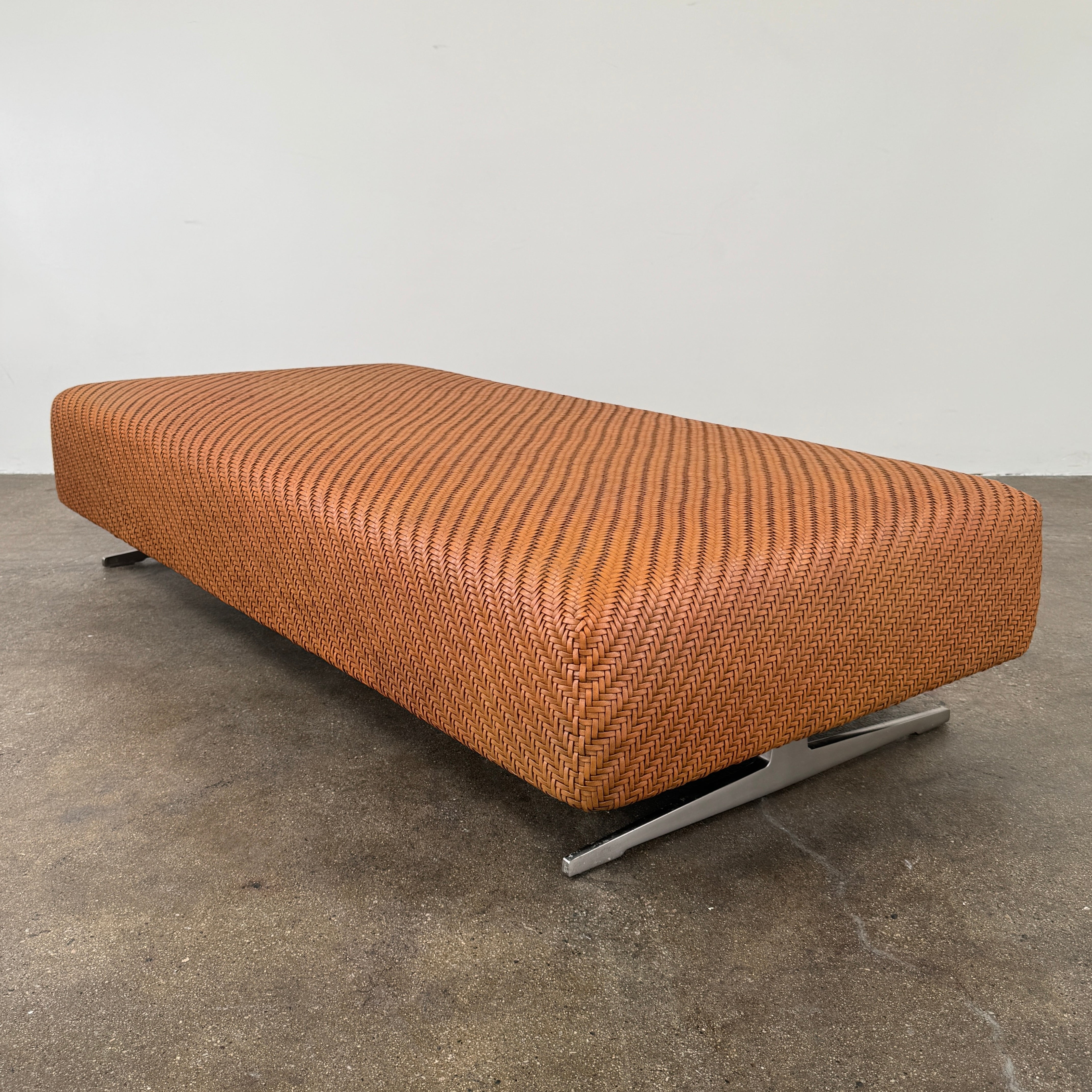 Flexform Filicudi Woven Pouf by Flexform, a rectangular orange bench with a low backless design and metal legs, displayed against a plain white background. Inspired by the iconic Filicudi collection, this elegant piece showcases a distinctive herringbone weave that adds texture and sophistication.