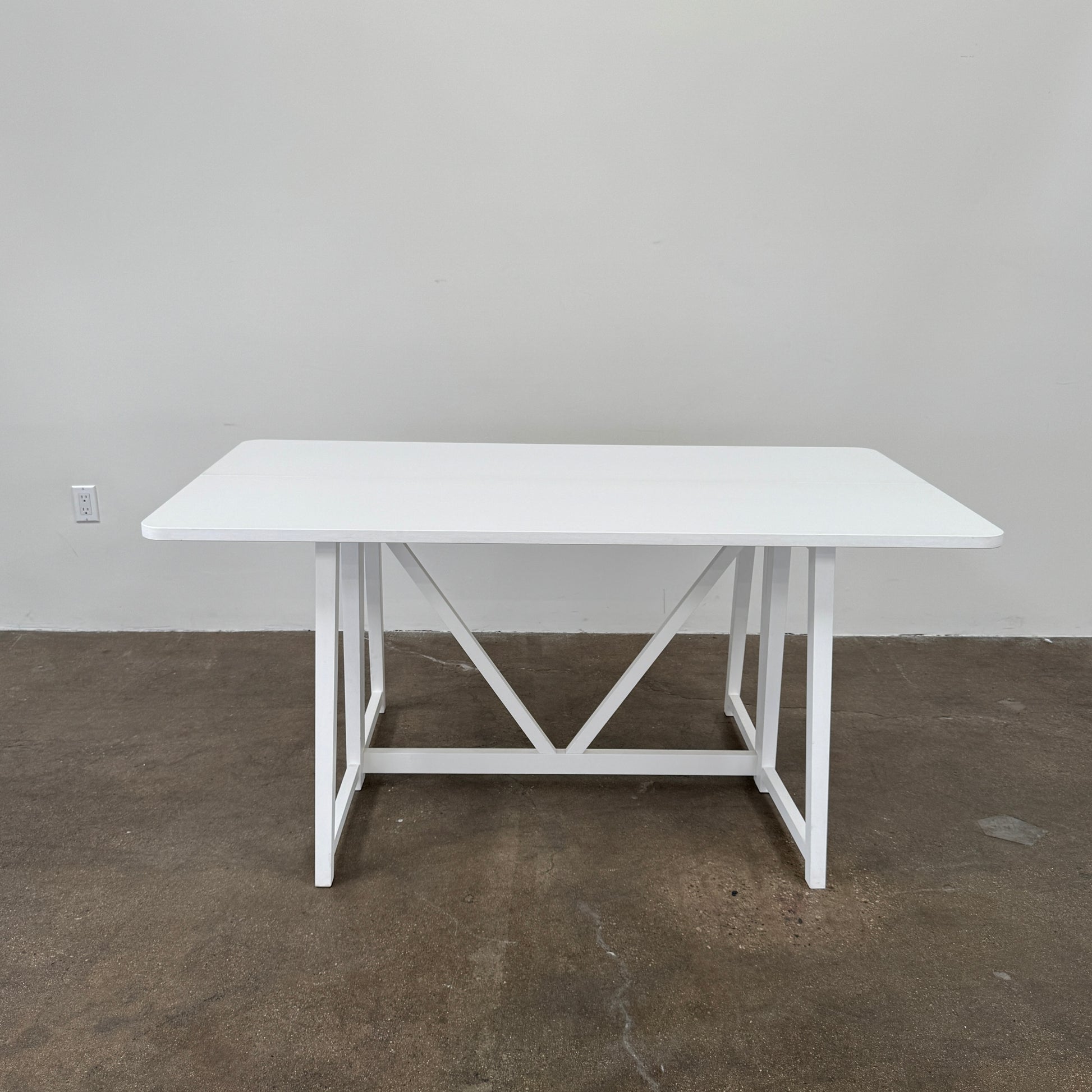 The Gervasoni Gray 51 Console/Table by Gervasoni, featuring a rectangular white design with a simple support frame, stands on a brown concrete floor against a plain white wall.