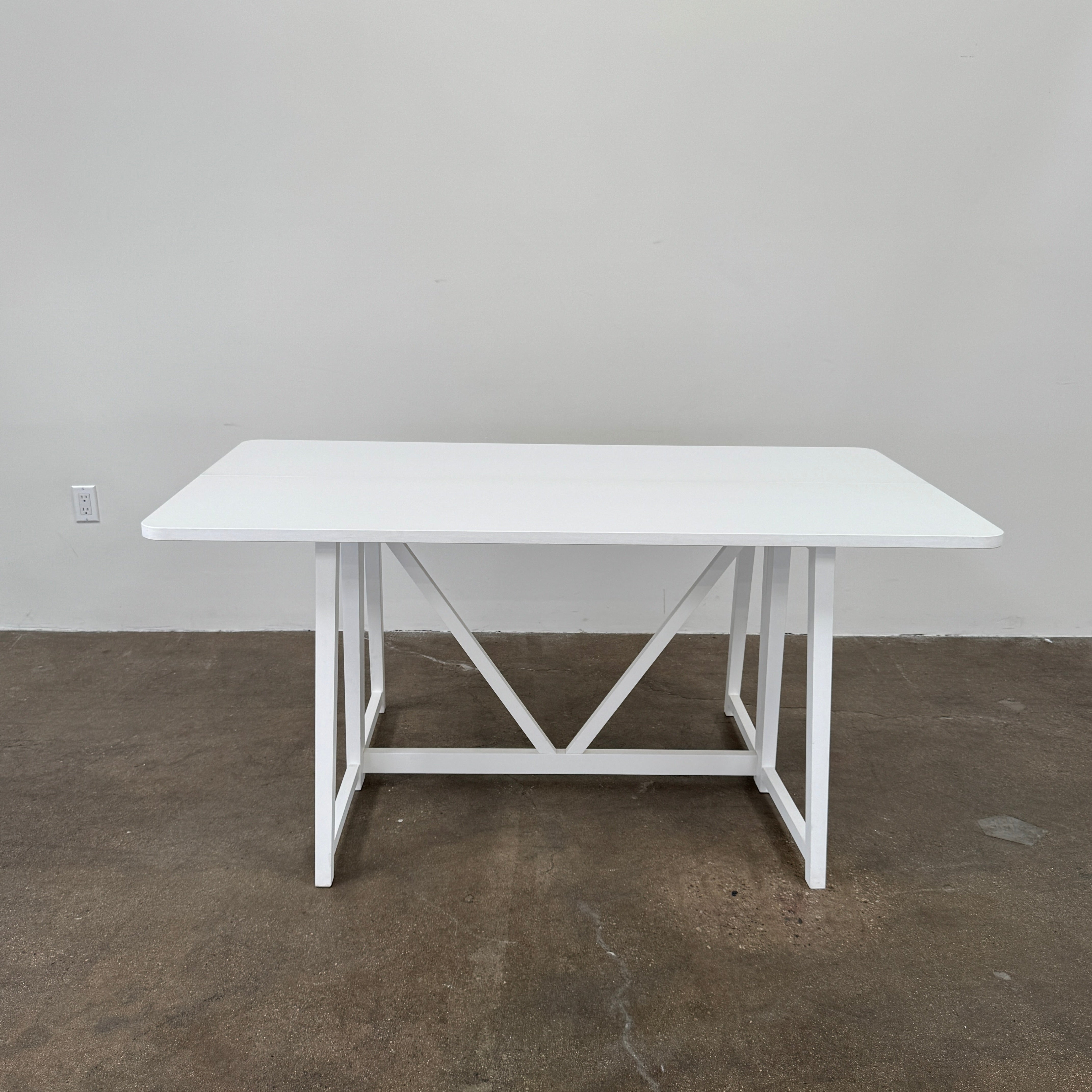 The Gervasoni Gray 51 Console/Table by Gervasoni, featuring a rectangular white design with a simple support frame, stands on a brown concrete floor against a plain white wall.
