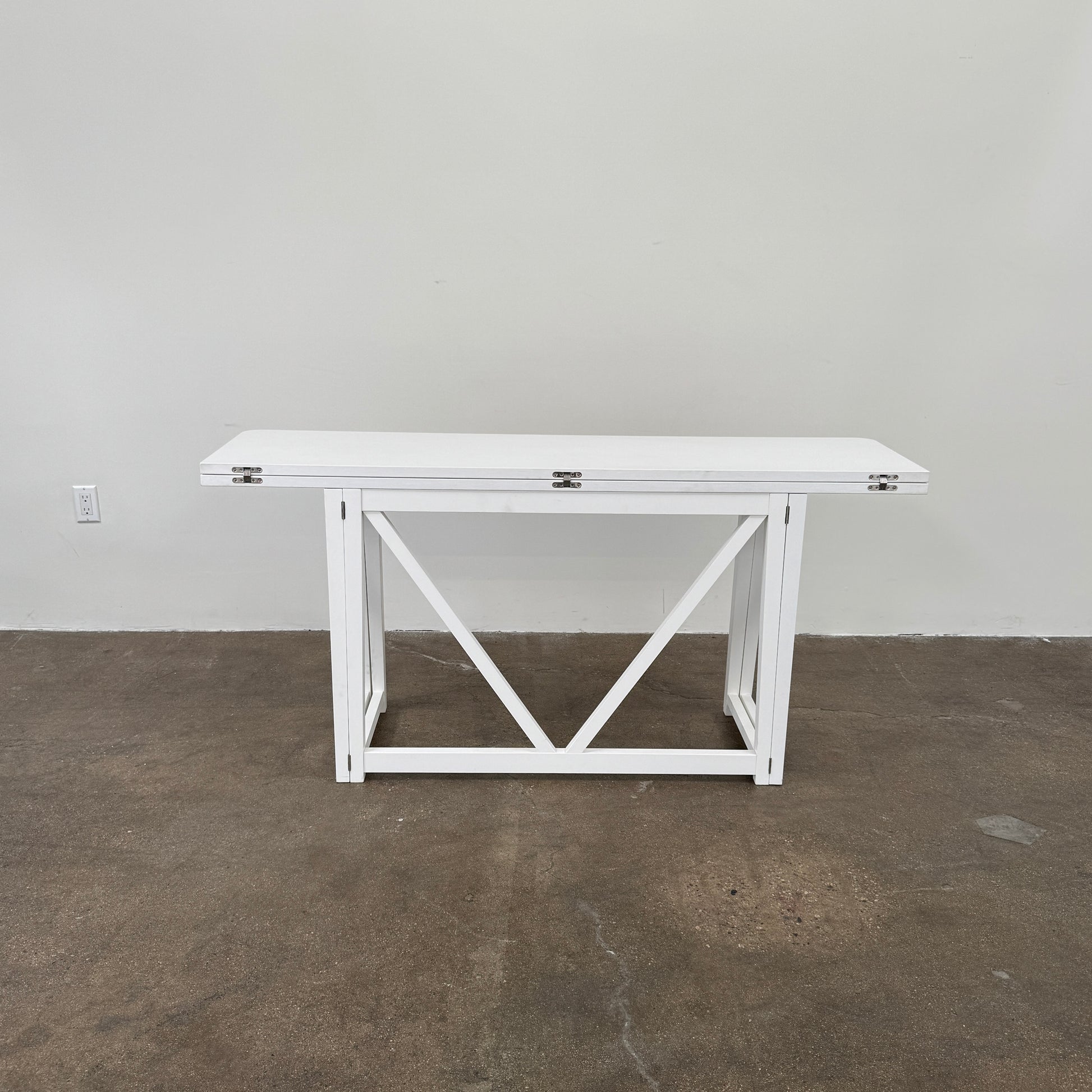 The Gervasoni Gray 51 Console/Table by Gervasoni, featuring a rectangular white design with a simple support frame, stands on a brown concrete floor against a plain white wall.