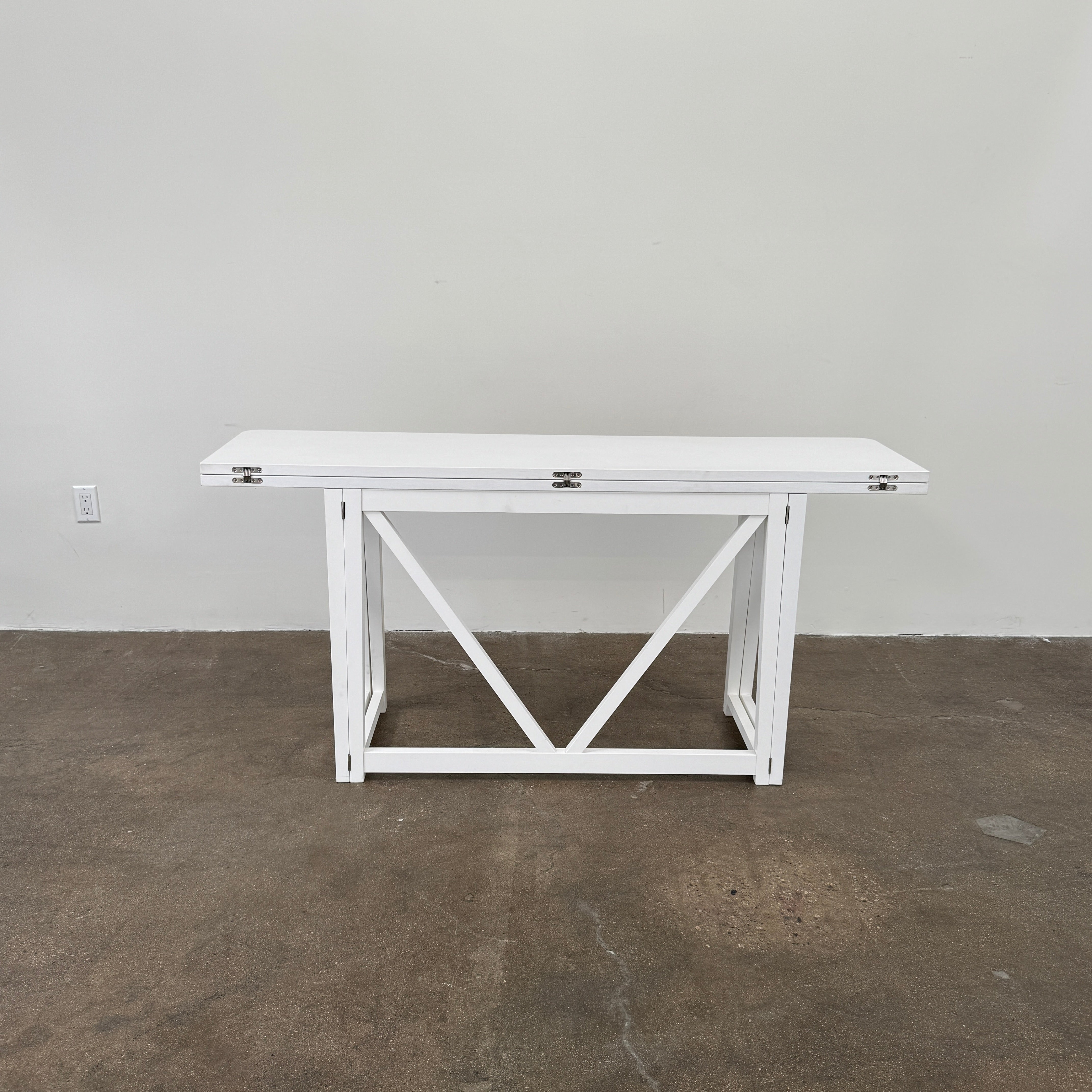 The Gervasoni Gray 51 Console/Table by Gervasoni, featuring a rectangular white design with a simple support frame, stands on a brown concrete floor against a plain white wall.