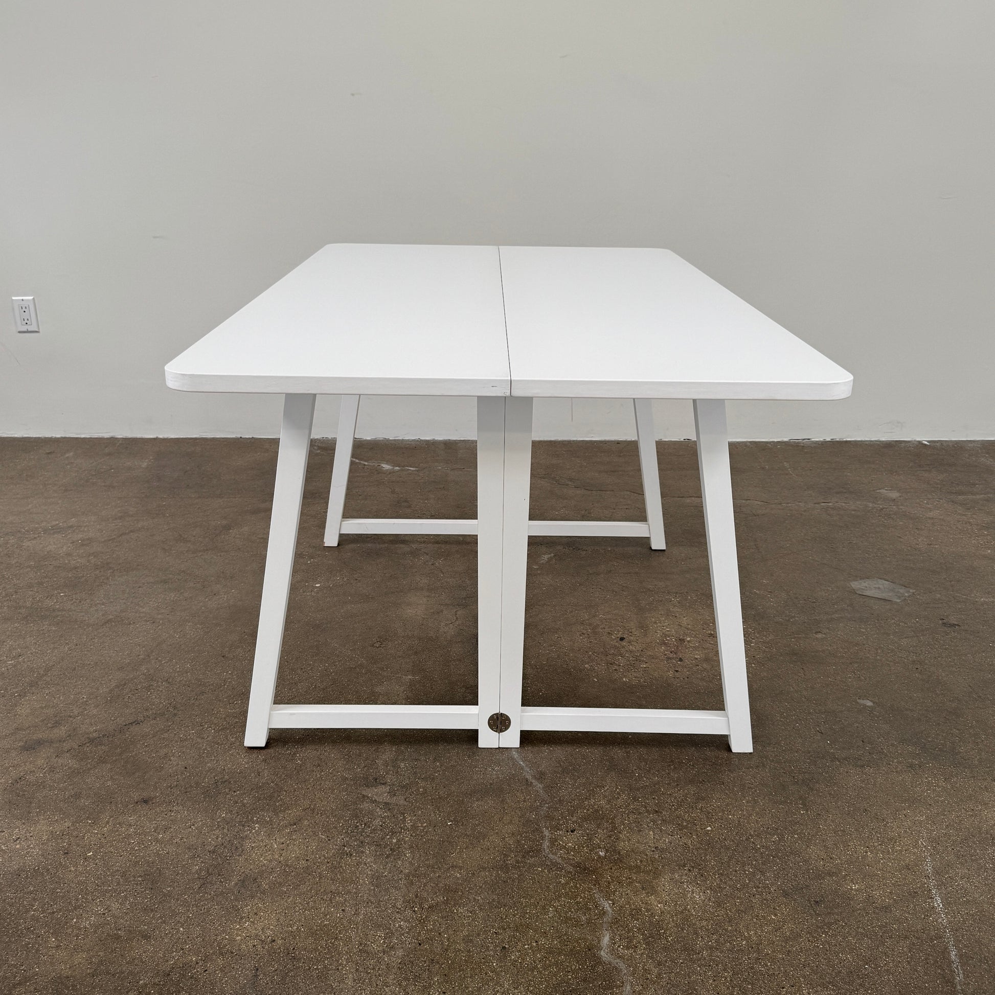 The Gervasoni Gray 51 Console/Table by Gervasoni, featuring a rectangular white design with a simple support frame, stands on a brown concrete floor against a plain white wall.