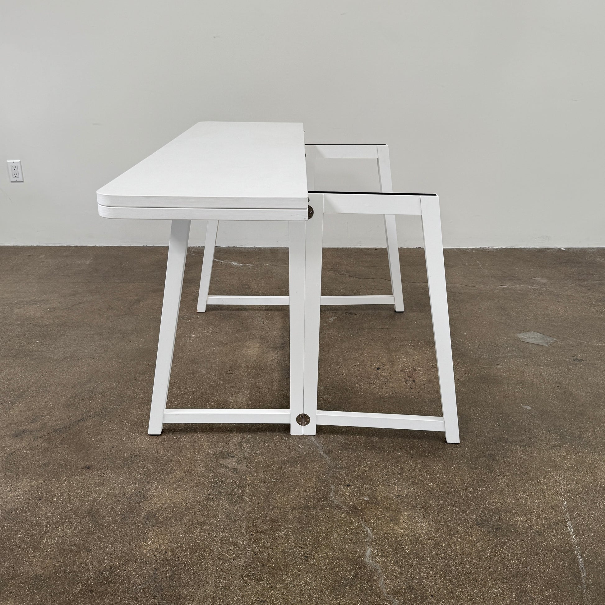The Gervasoni Gray 51 Console/Table by Gervasoni, featuring a rectangular white design with a simple support frame, stands on a brown concrete floor against a plain white wall.