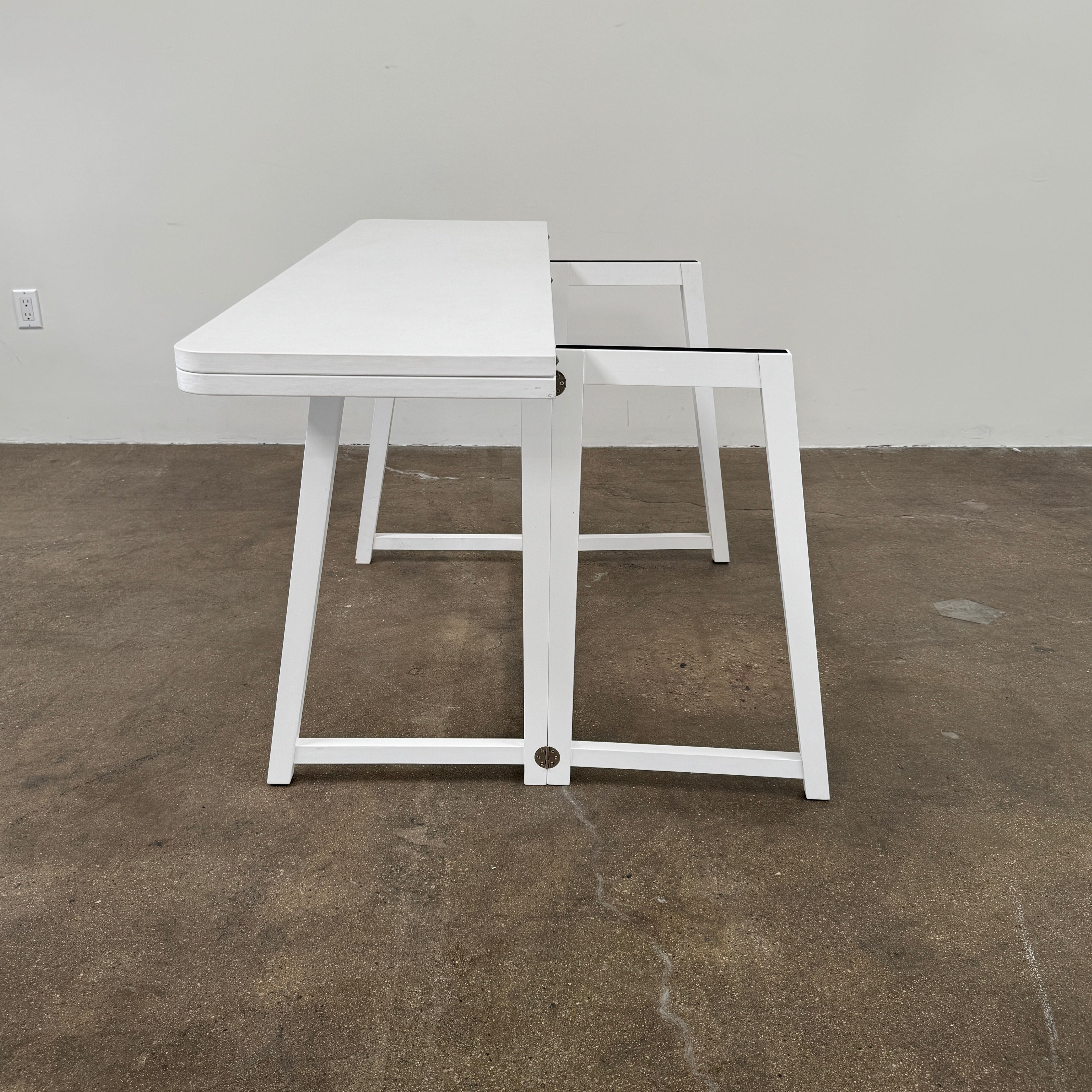 The Gervasoni Gray 51 Console/Table by Gervasoni, featuring a rectangular white design with a simple support frame, stands on a brown concrete floor against a plain white wall.