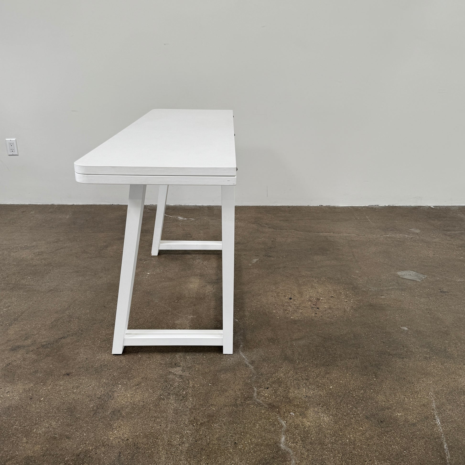 The Gervasoni Gray 51 Console/Table by Gervasoni, featuring a rectangular white design with a simple support frame, stands on a brown concrete floor against a plain white wall.