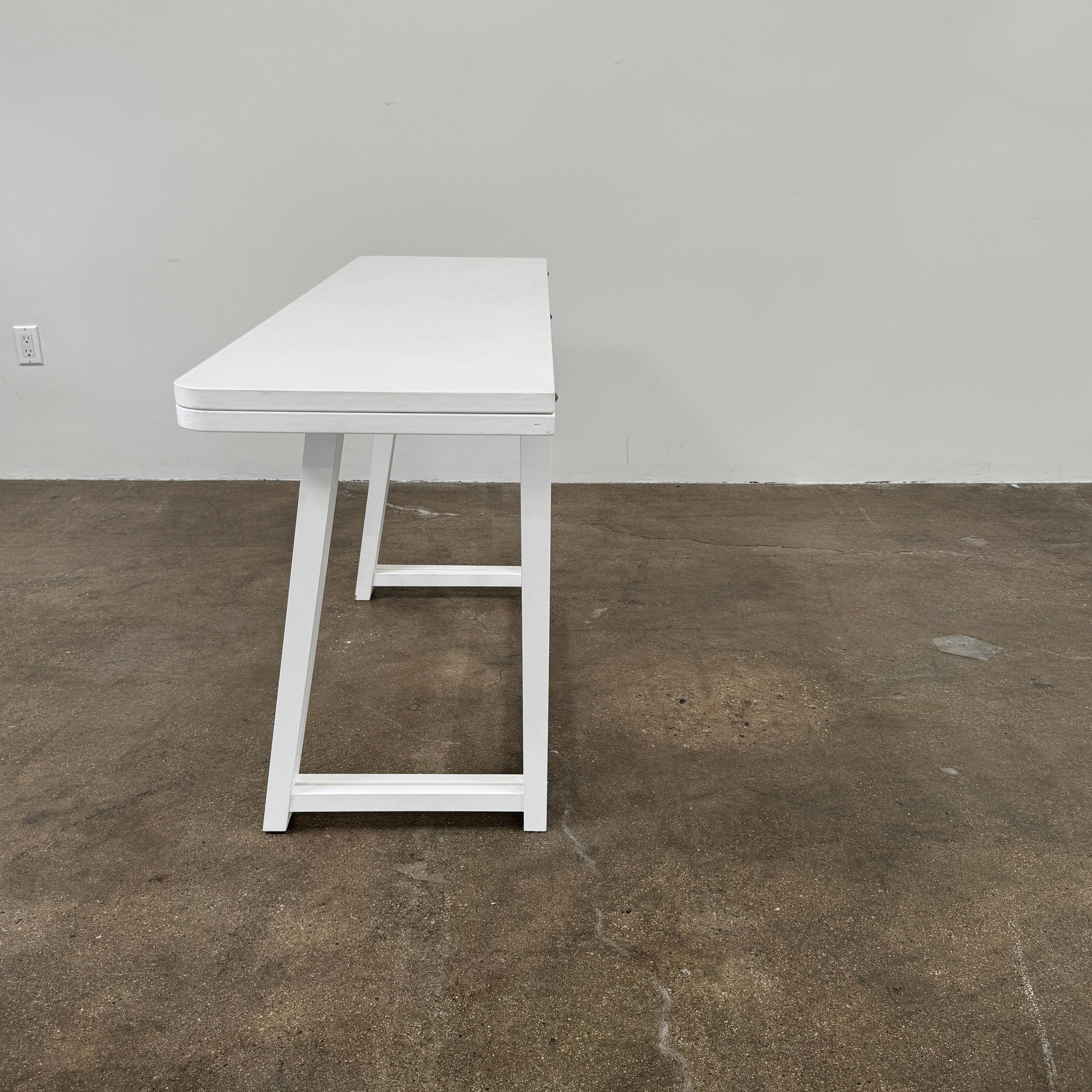 The Gervasoni Gray 51 Console/Table by Gervasoni, featuring a rectangular white design with a simple support frame, stands on a brown concrete floor against a plain white wall.
