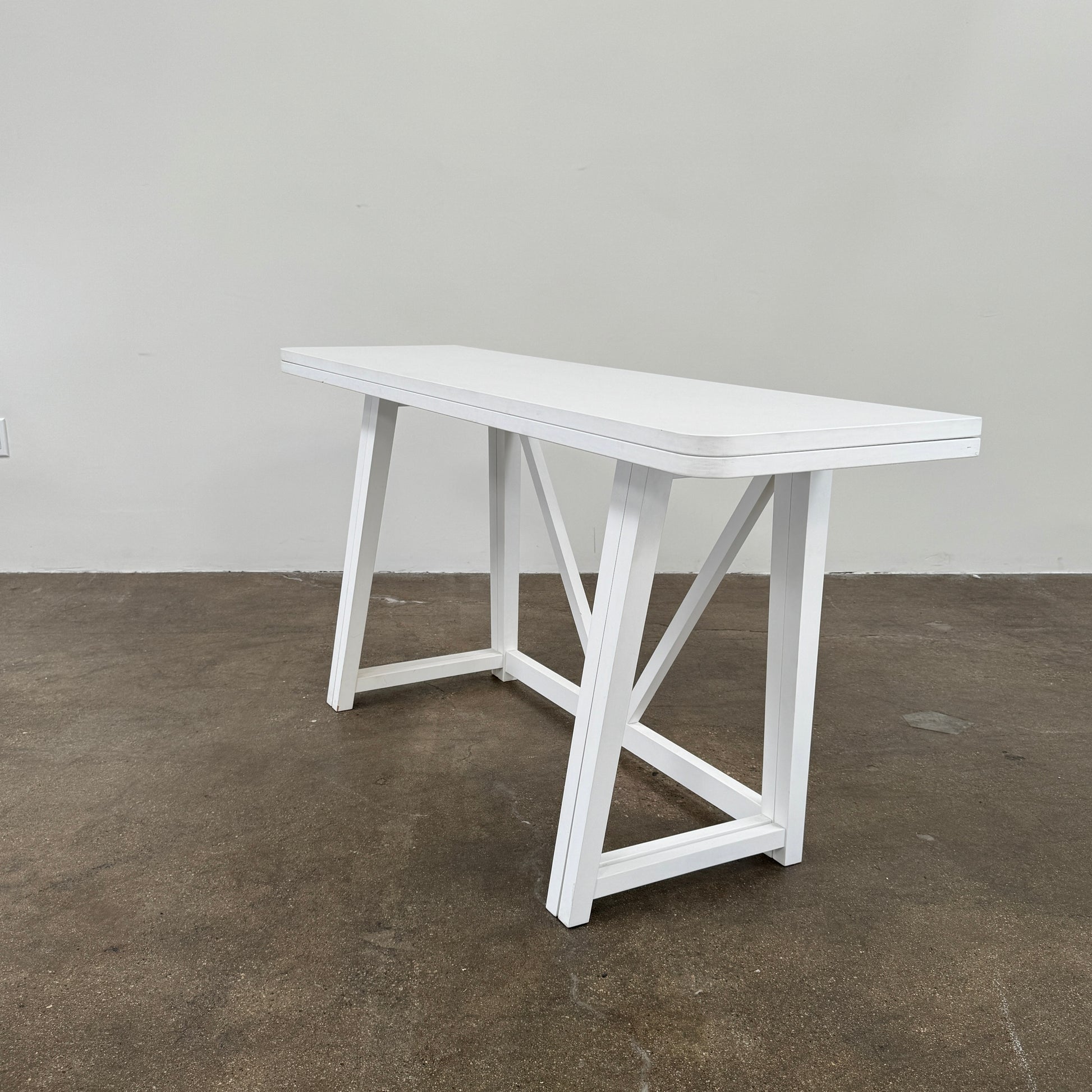 The Gervasoni Gray 51 Console/Table by Gervasoni, featuring a rectangular white design with a simple support frame, stands on a brown concrete floor against a plain white wall.