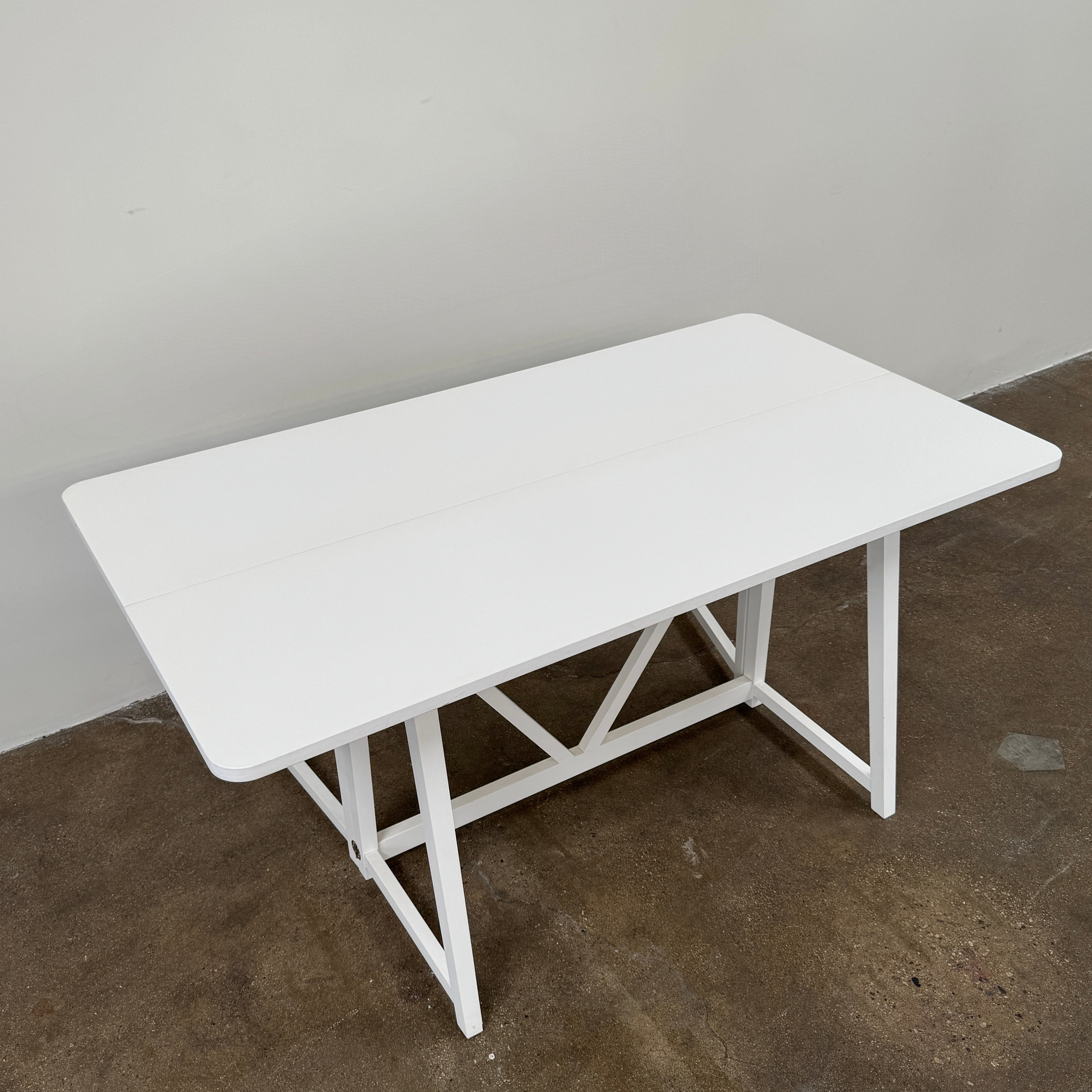 The Gervasoni Gray 51 Console/Table by Gervasoni, featuring a rectangular white design with a simple support frame, stands on a brown concrete floor against a plain white wall.