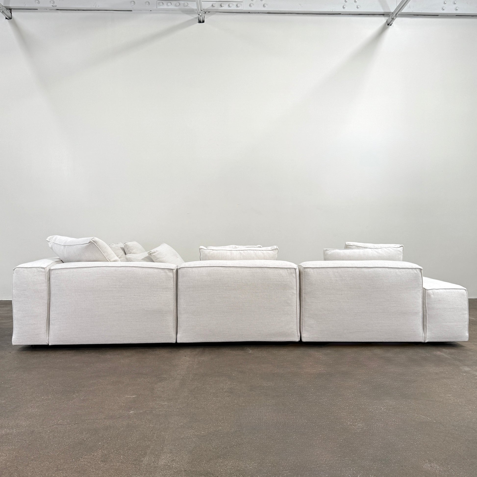 The Living Divani NeoWall 4 piece Modular Sofa by Living Divani is a modern, light beige Italian modular sofa featuring six large seat cushions and seven matching throw pillows, displayed against a white background.