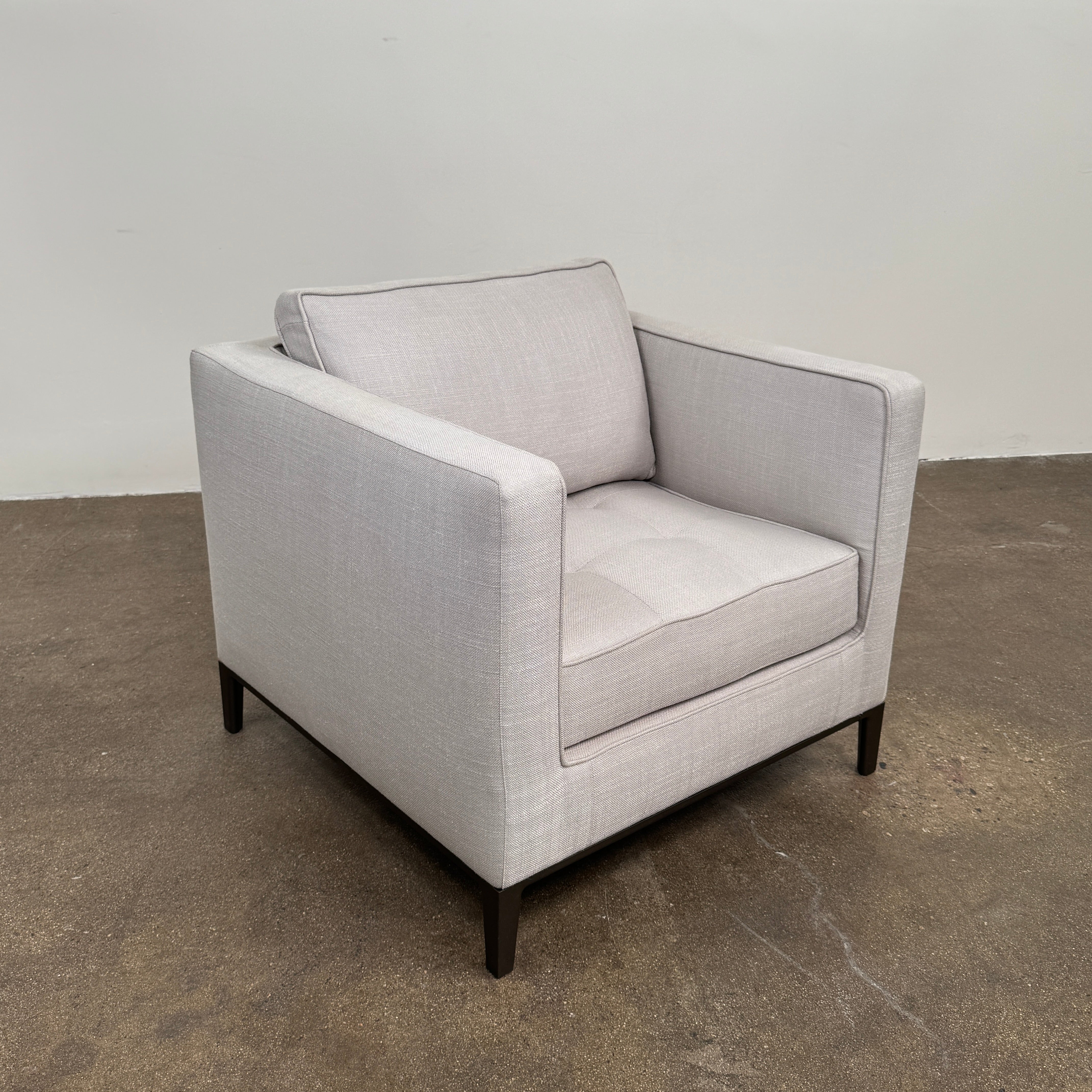 A modern Maxalto Lucrezia Soft Armchair in light gray, featuring square arms, a cushioned seat and back, and dark wooden legs from Maxalto, showcases refined design and plush comfort against a plain white background.