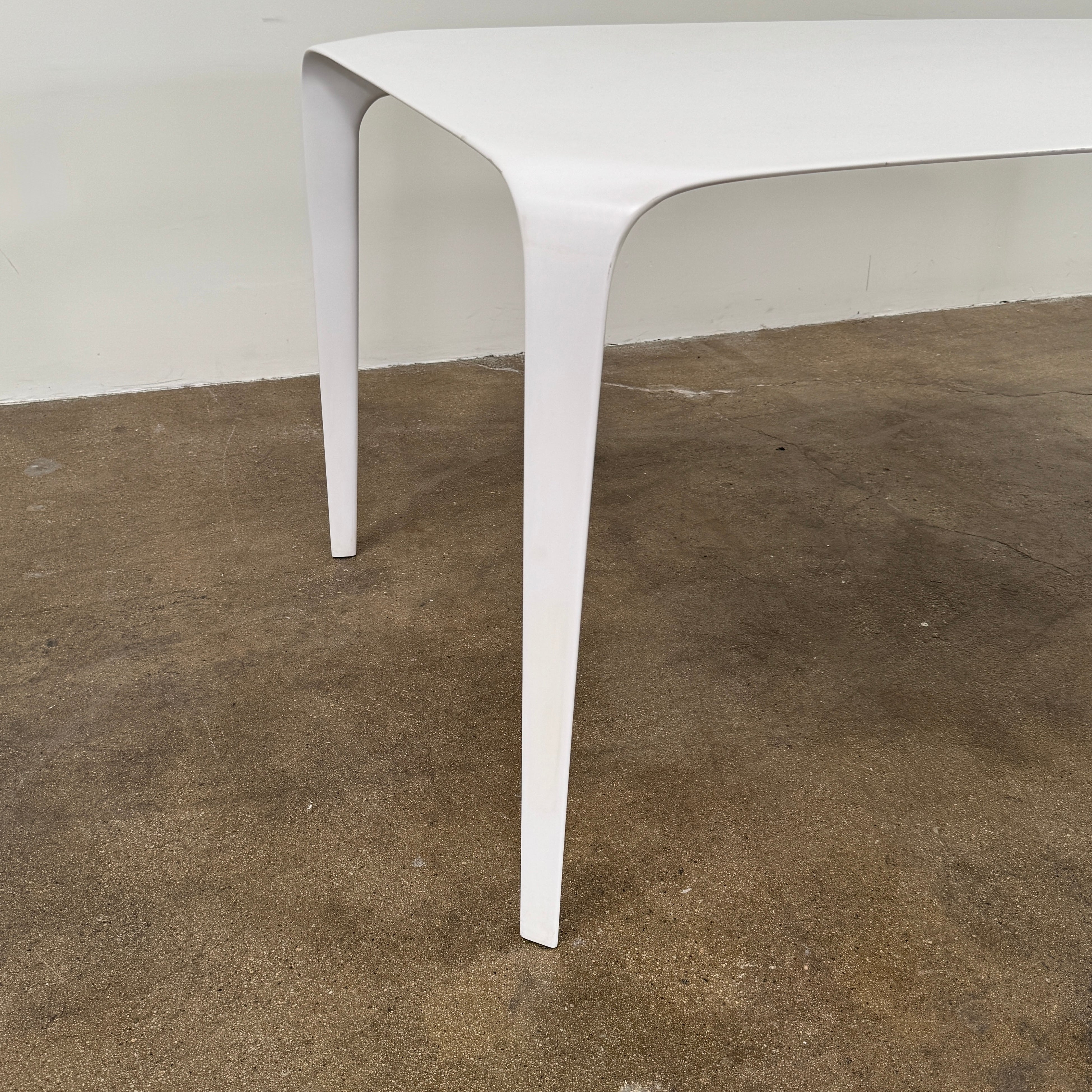 A modern white rectangular B&B Italia LINK Indoor / Outdoor Dining Table by B&B Italia, featuring rounded edges, stands on a brown concrete floor against a plain light gray wall.