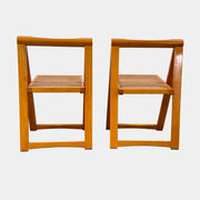 A set of 2 Vintage Aldo Jacober Folding Chairs, featuring wooden frames and woven rattan seats, are positioned side by side on a concrete floor against a plain white wall, shown from the back.