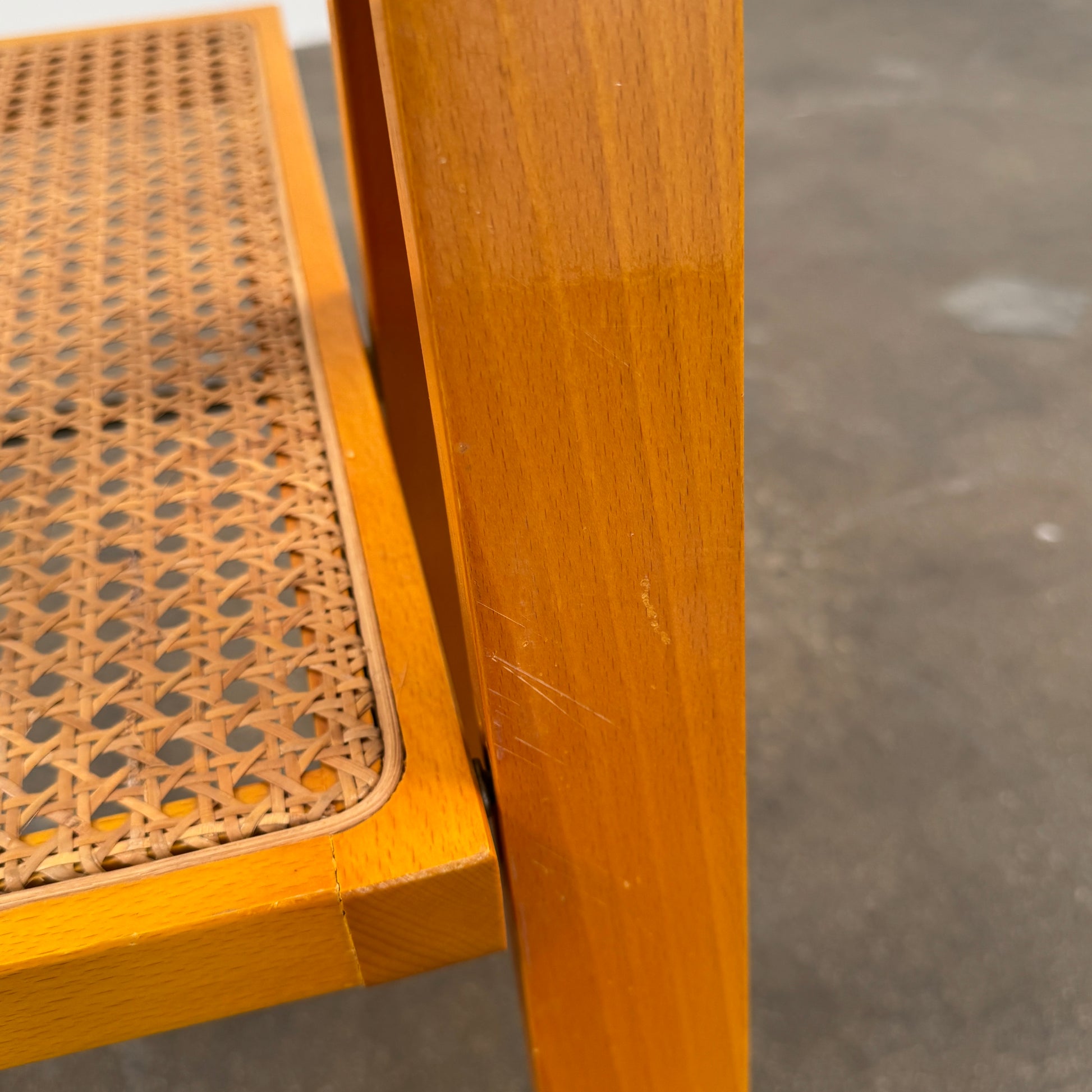 A set of 2 Vintage Aldo Jacober Folding Chairs, featuring wooden frames and woven rattan seats, are positioned side by side on a concrete floor against a plain white wall, shown from the back.