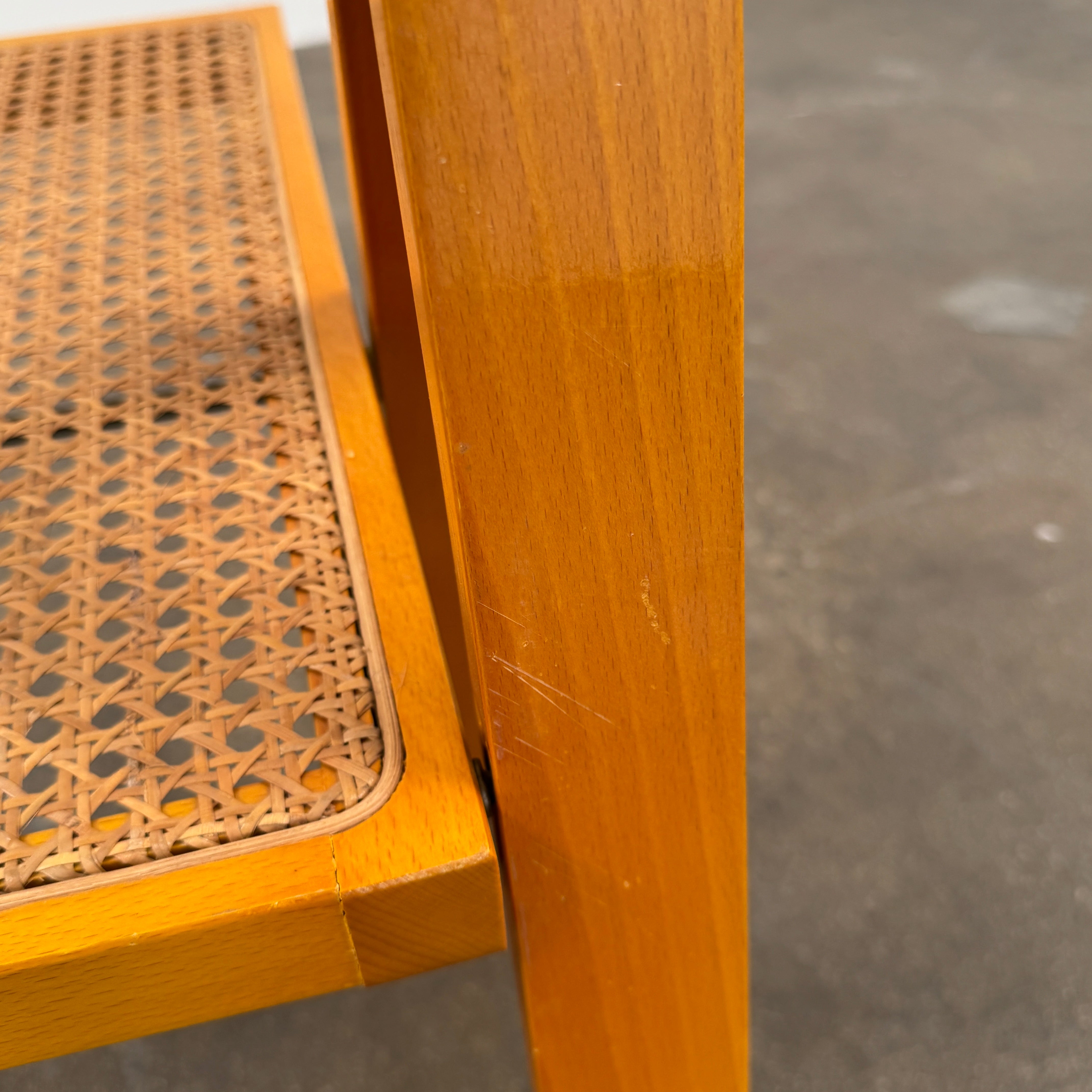 A set of 2 Vintage Aldo Jacober Folding Chairs, featuring wooden frames and woven rattan seats, are positioned side by side on a concrete floor against a plain white wall, shown from the back.