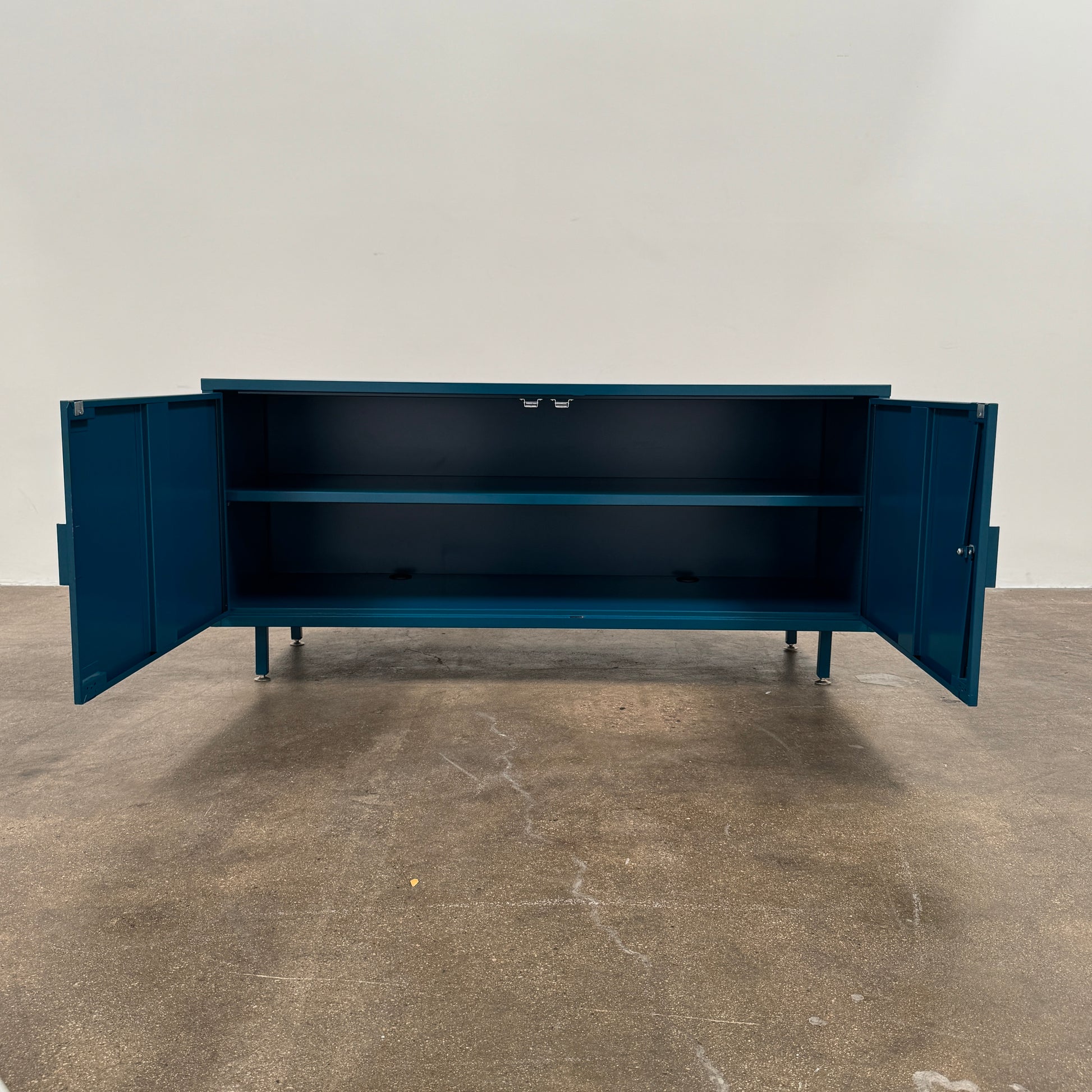 A blue metal Heartwork Active Duty Storage Credenza with two doors, a central lock, and four legs stands against a plain white background—this Heartwork piece offers durable construction ideal for workplace storage.