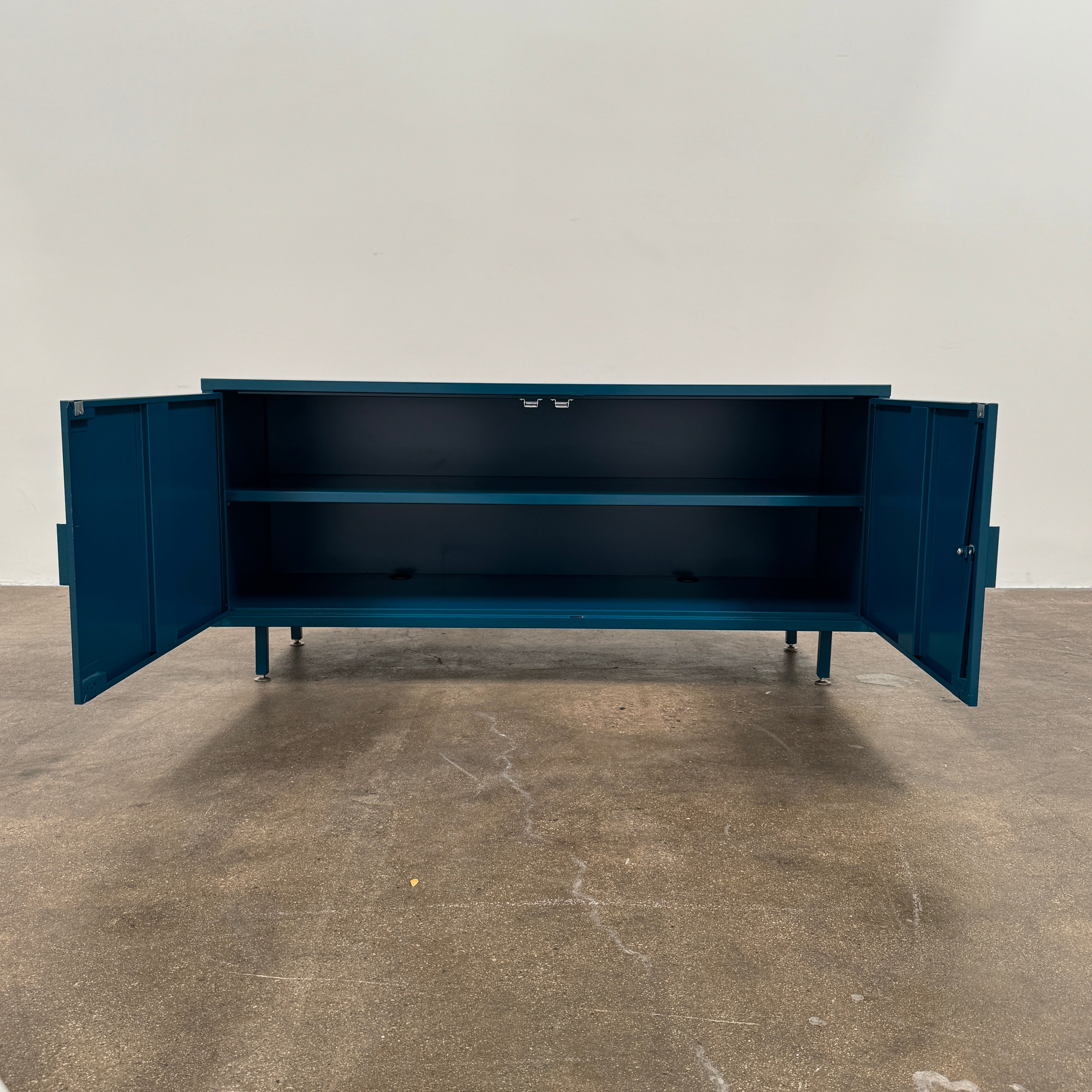 A blue metal Heartwork Active Duty Storage Credenza with two doors, a central lock, and four legs stands against a plain white background—this Heartwork piece offers durable construction ideal for workplace storage.
